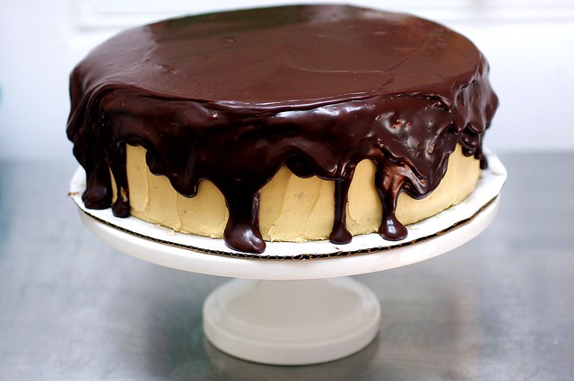 A cake dripping in chocolate ganache glaze sits on a cake platter.