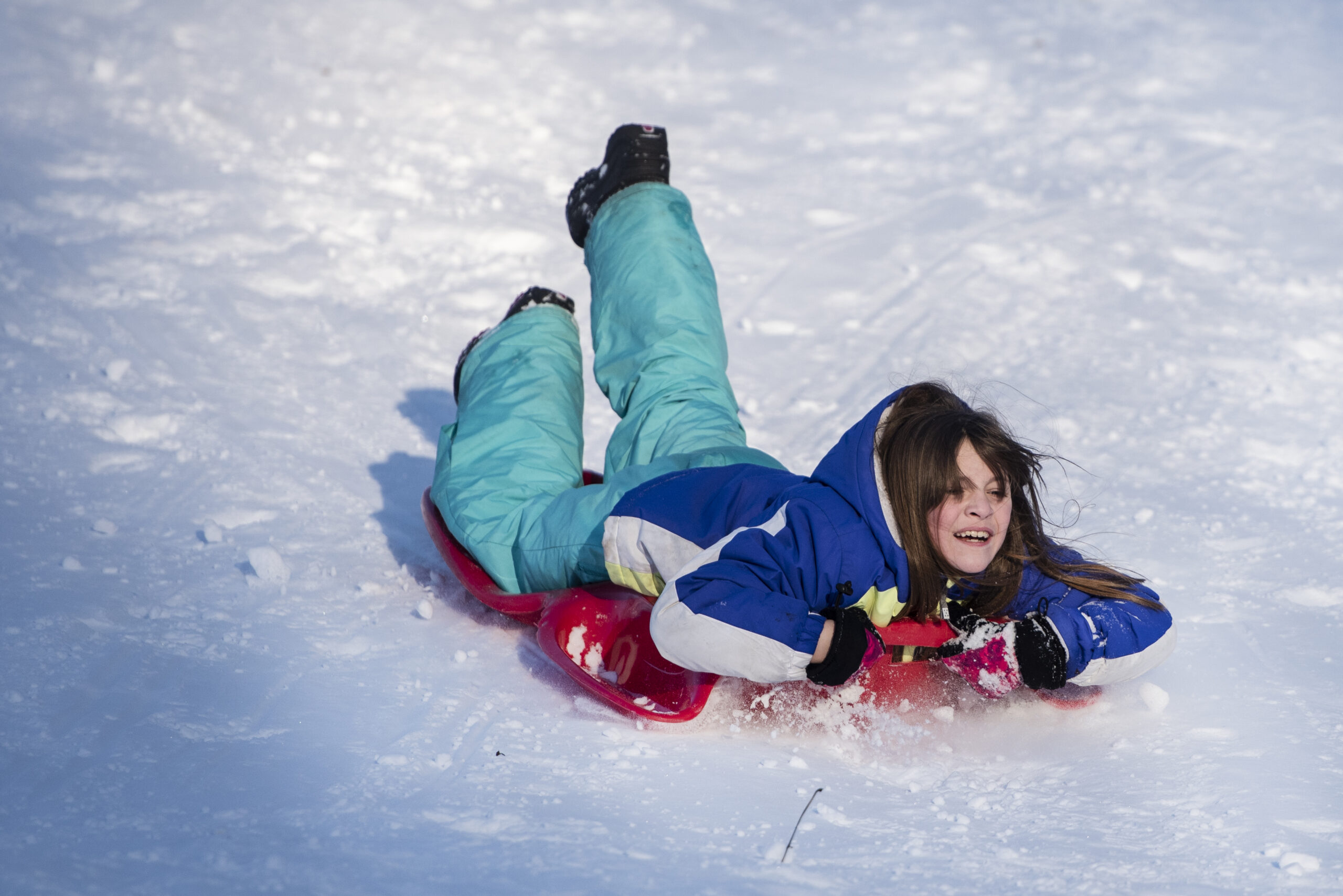 A girl smiles as she sleds down a hill on a red sled