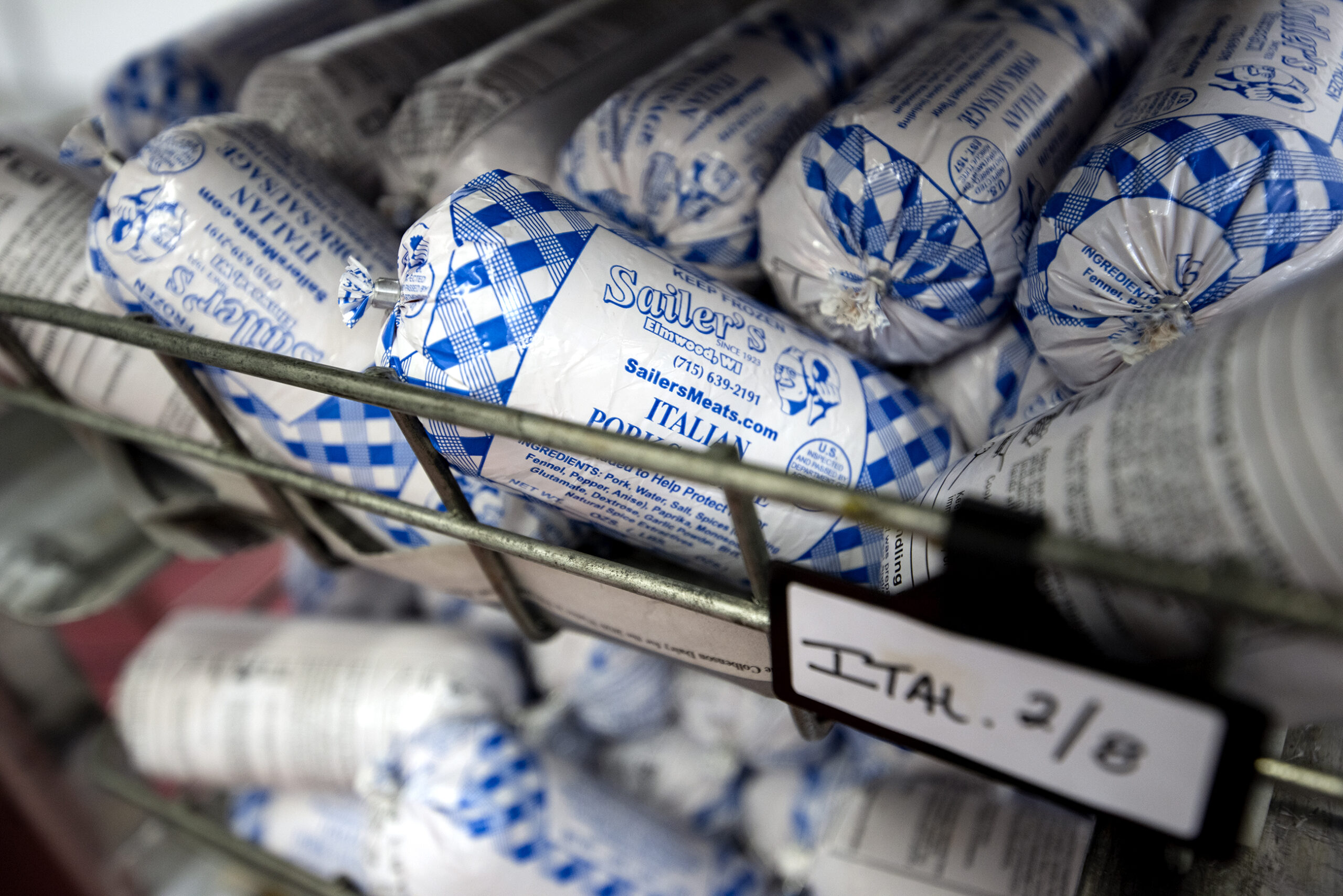 Blue and white packaged sausage is stored in a wire basket.