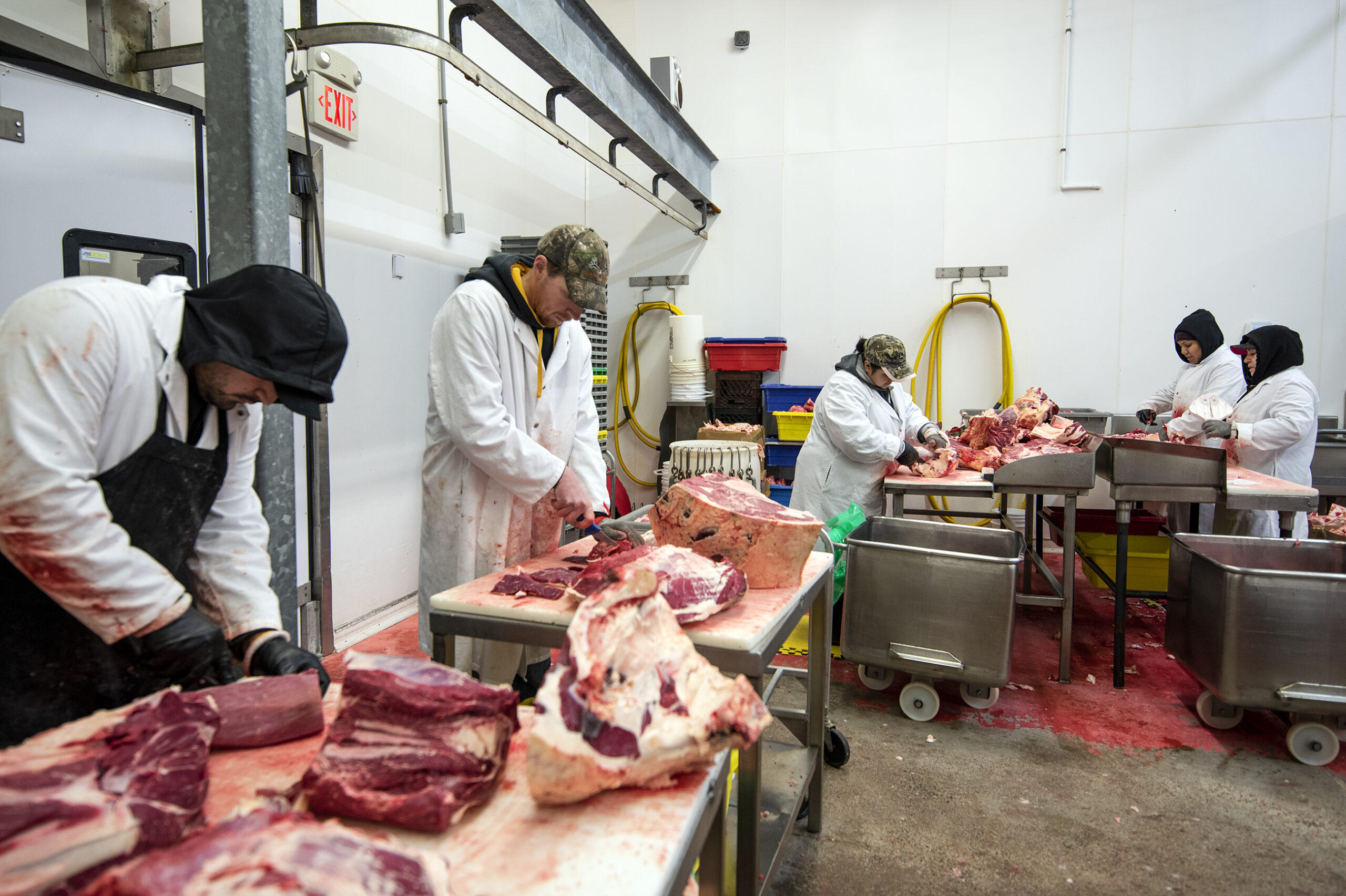 Five workers process meat at tables