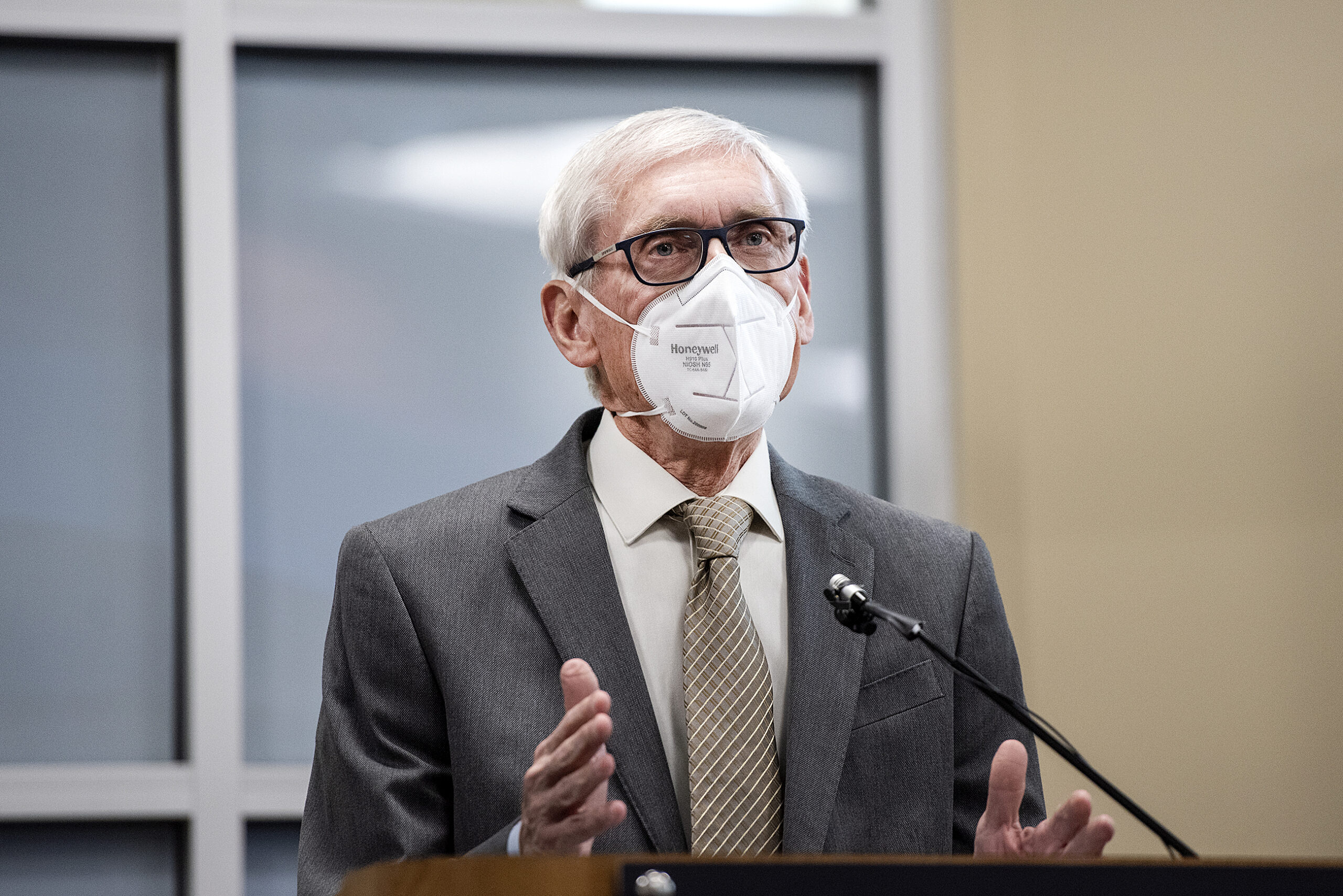 Gov. Evers speaks at a lectern while wearing a white face mask.