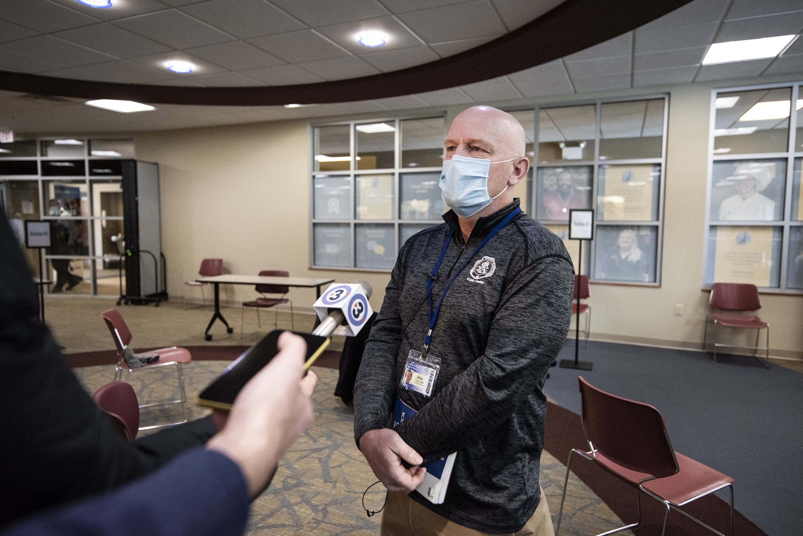 A man stands as he answers questions from reporters whose arms reach out toward him with microphones.