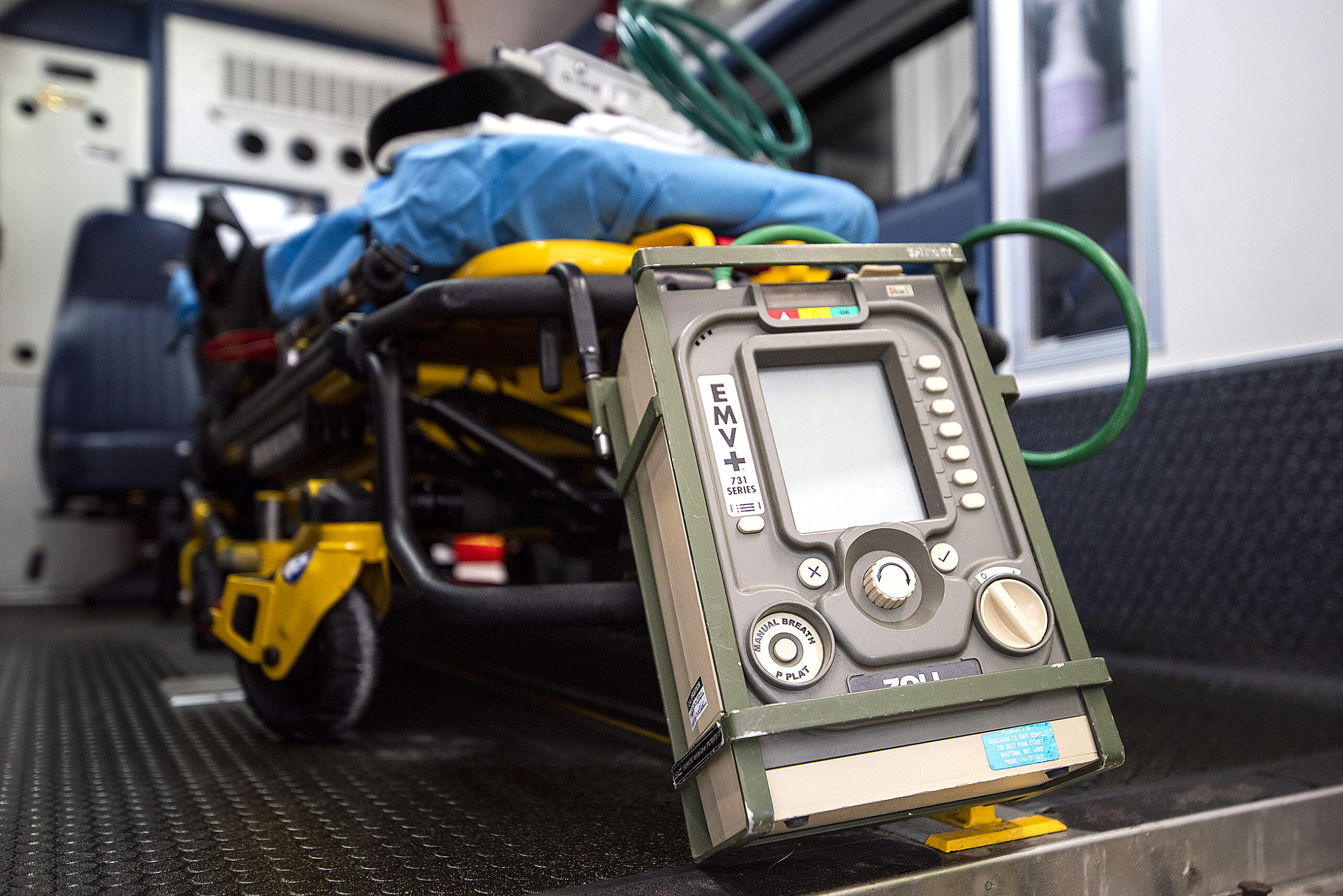 A ventilator with a screen and many buttons and knobs is placed in the back of an ambulance.