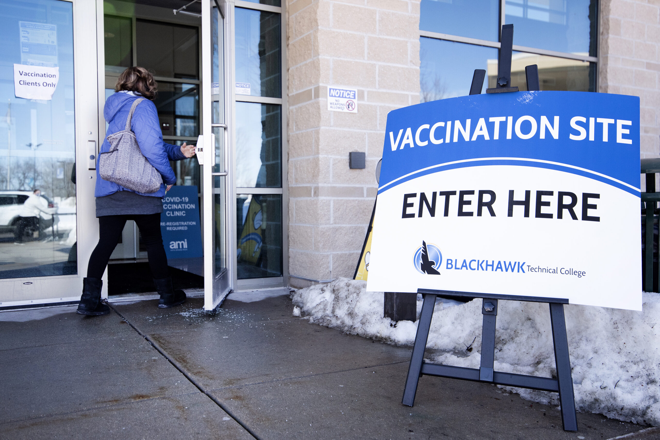 A person in a coat enters through glass doors near a sign that says 