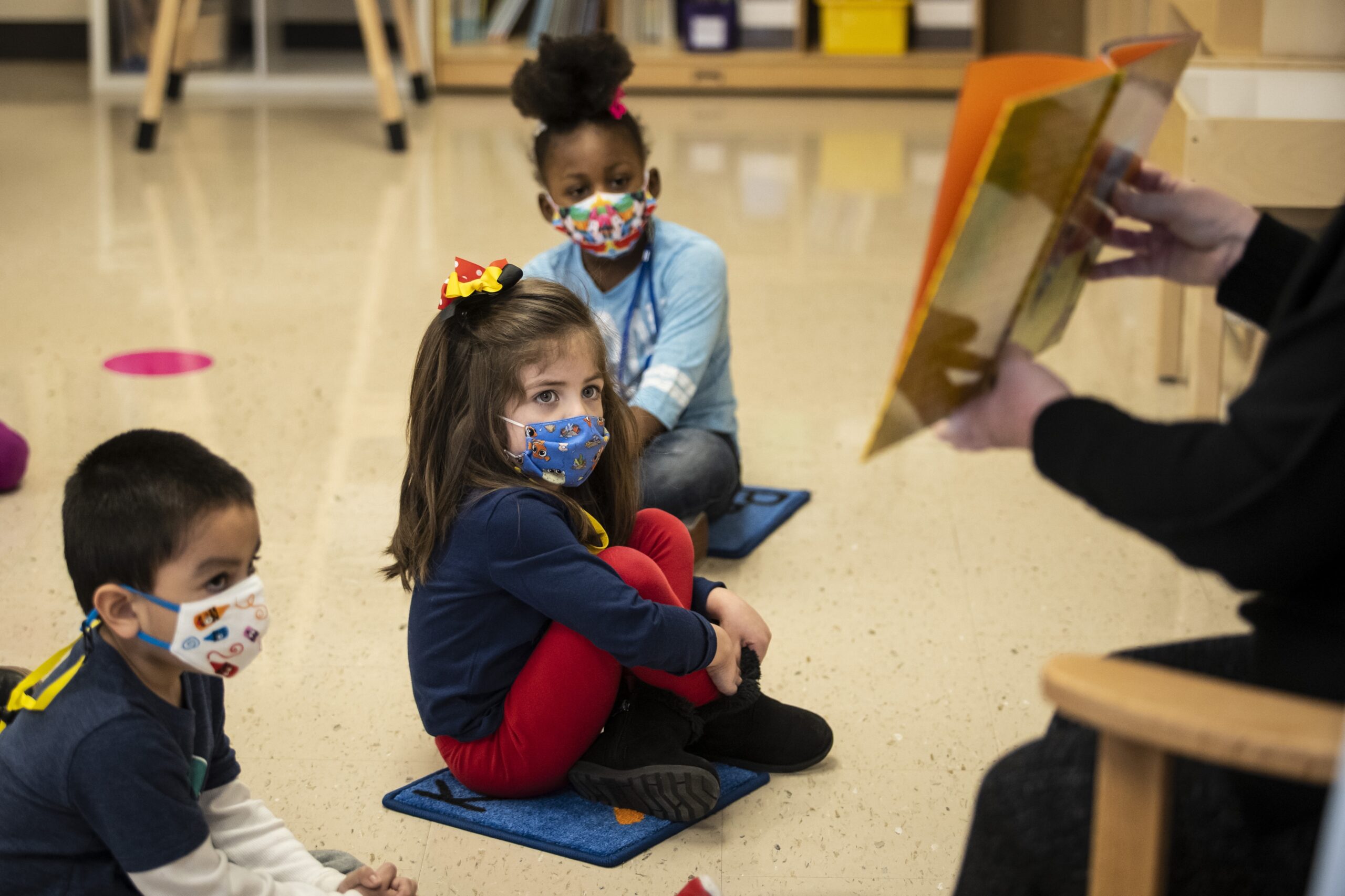 Pre-kindergarten students, in masks, listen as their teacher reads a story