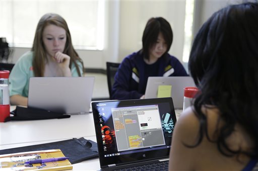 High School girls  work at laptops in a classroom wearing faces of concentration.