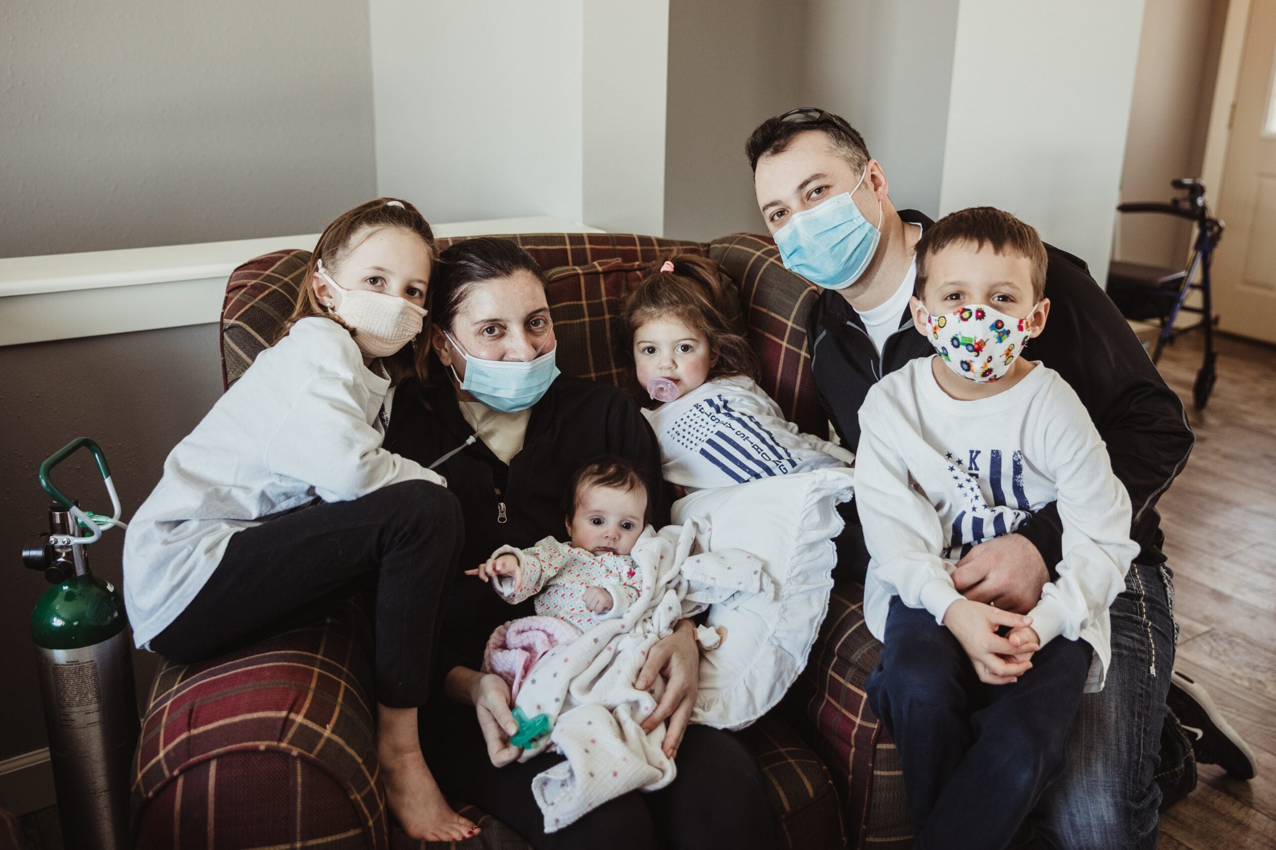 Man, woman and four children in masks sit on sofa