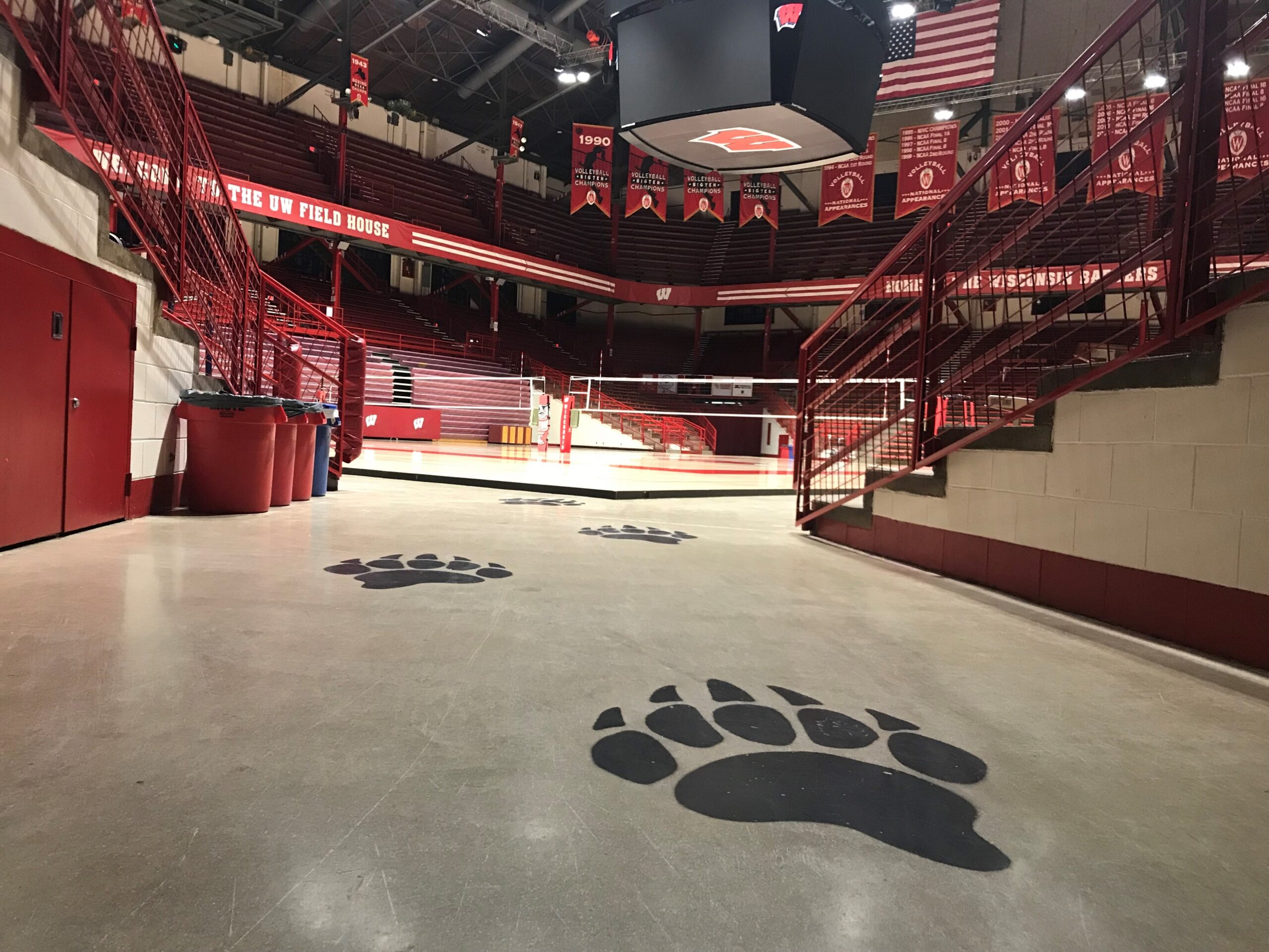 Big, black badger footprints painted on the floor lead to a volleyball court. The arena is all Wisconsin red and white.