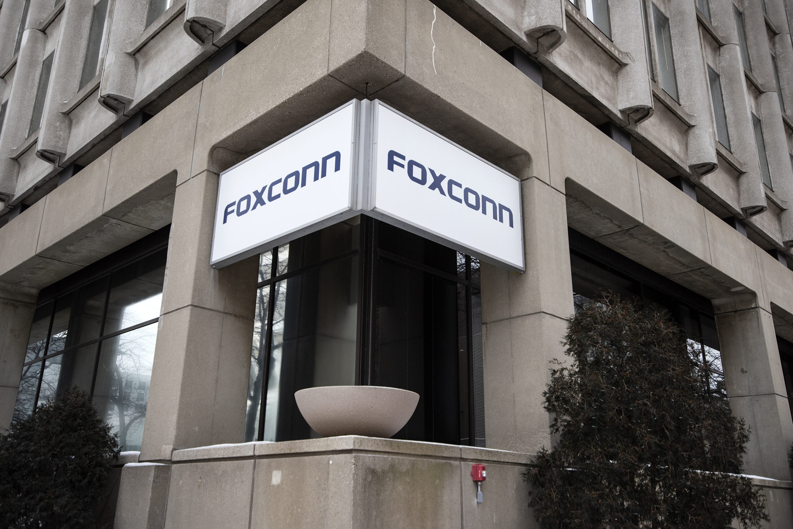 A white sign with the word "Foxconn" on it hangs on a concrete building.