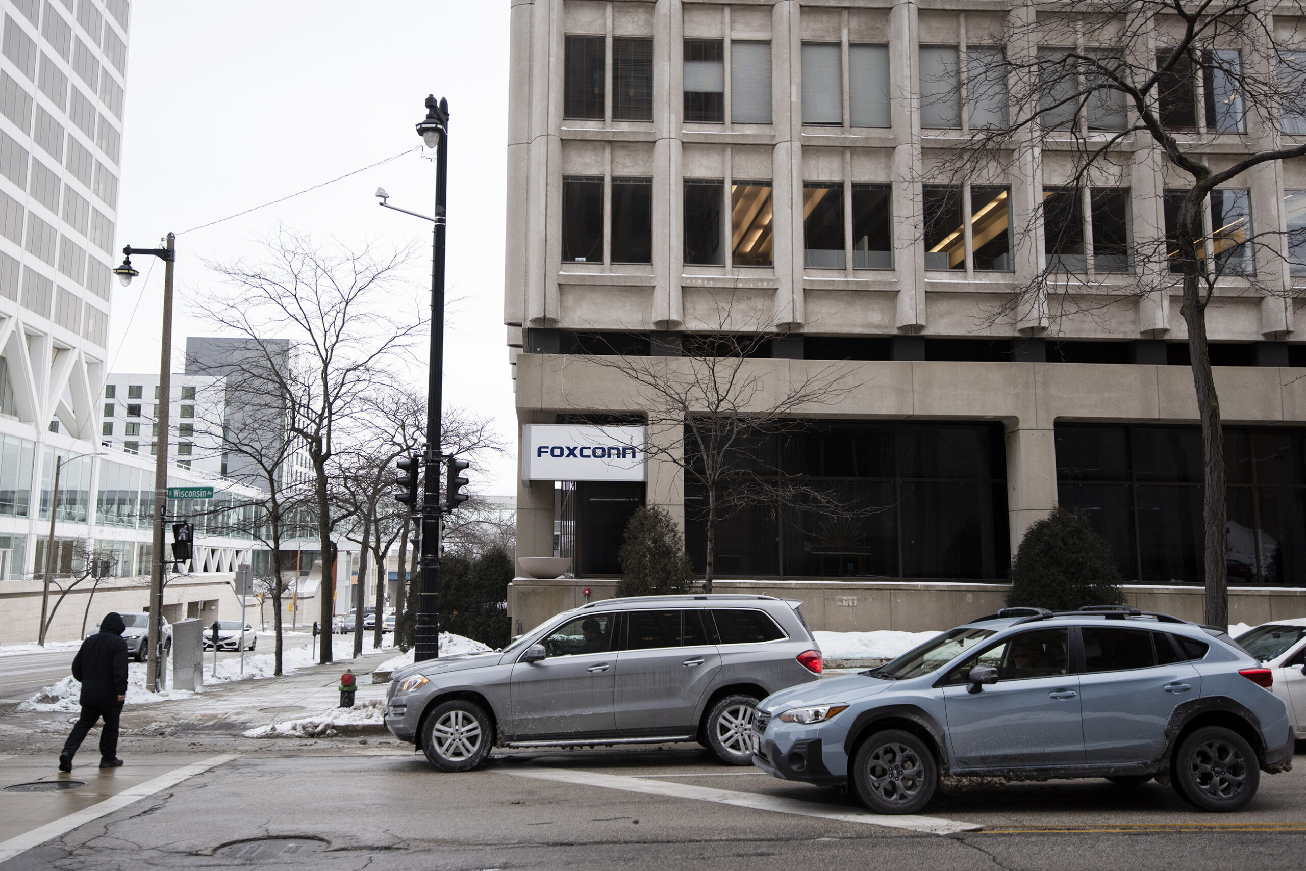 Cars wait for a pedestrian to cross the street in front of the beige Foxconn headquarters building.