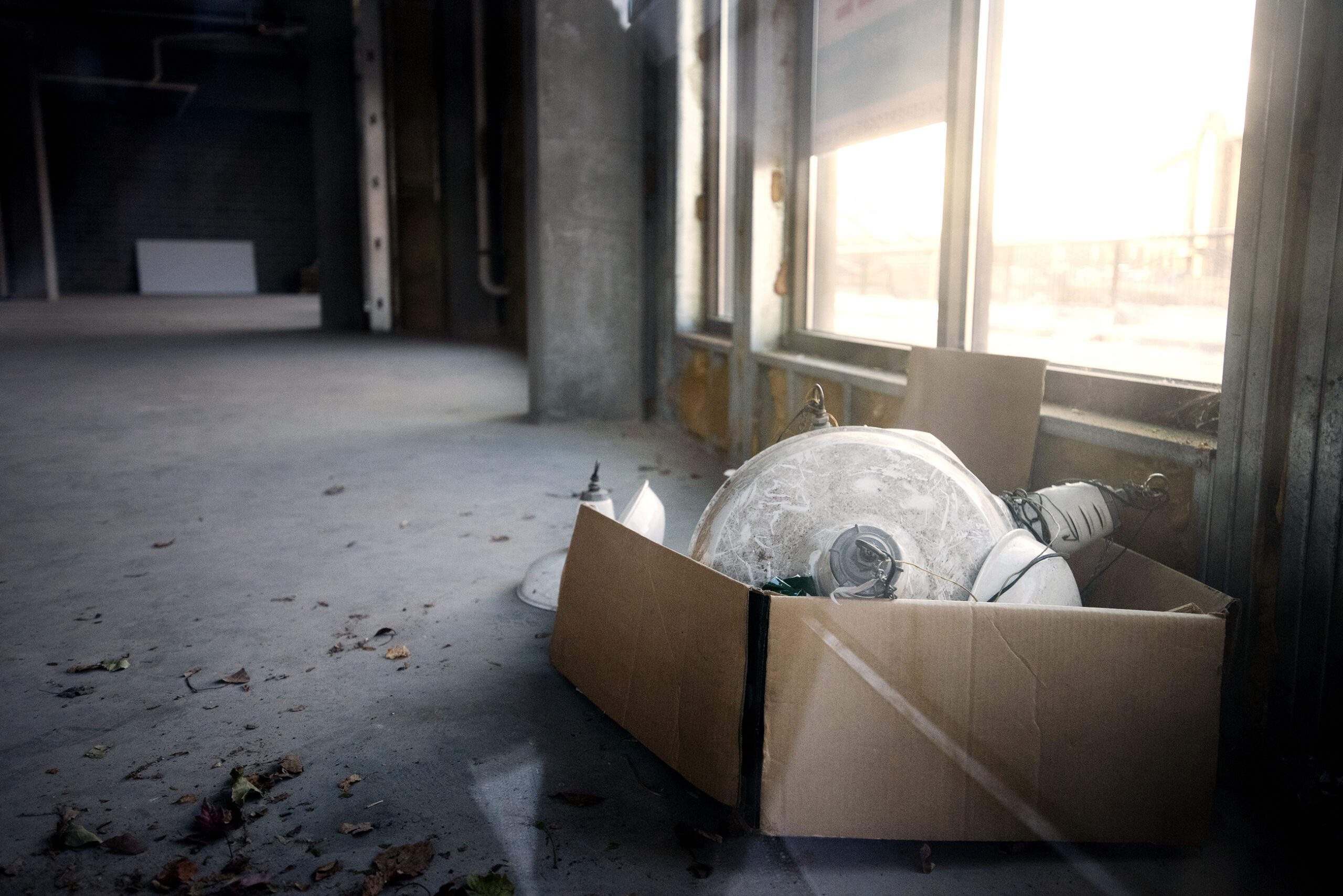 A cardboard box with various light fixtures inside sits on the concrete floor of a vacant room.