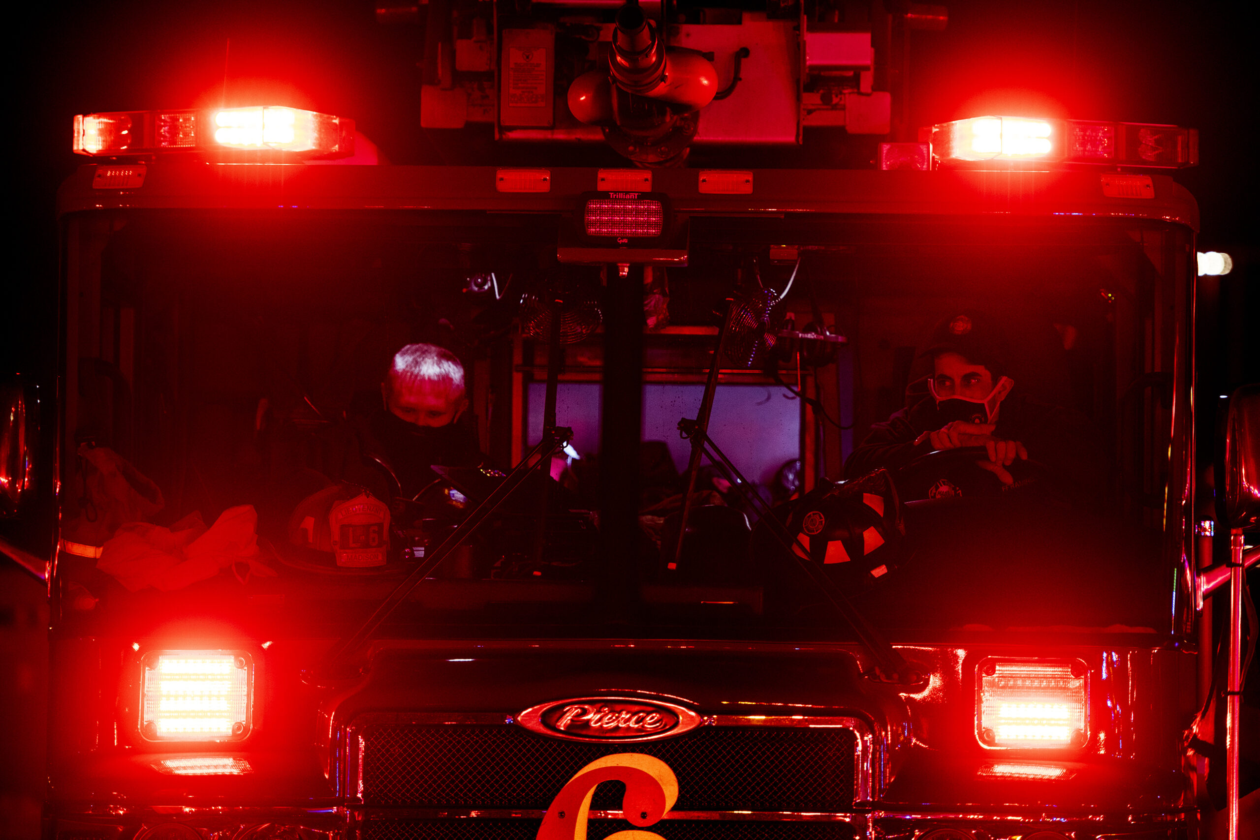 Four bright red lights glow into the night from a firetruck where firefighters are sitting.