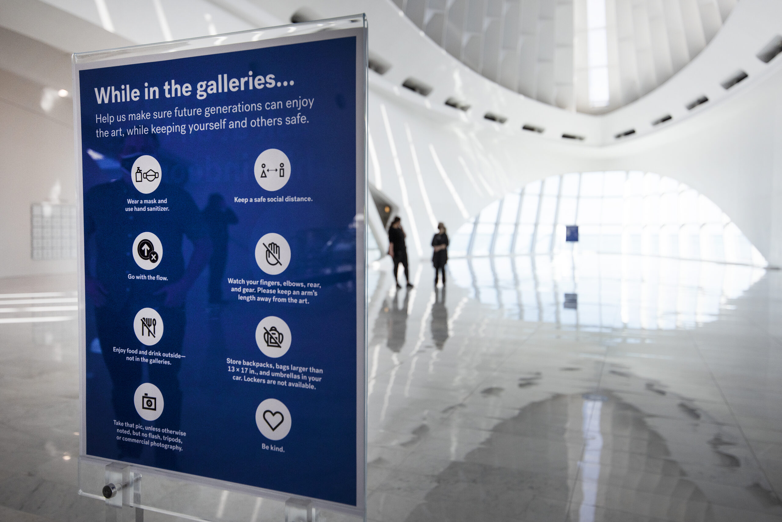 A blue sign is seen in the front of the museum begins with "While in the galleries..." and then explains COVID-19 safety rules.