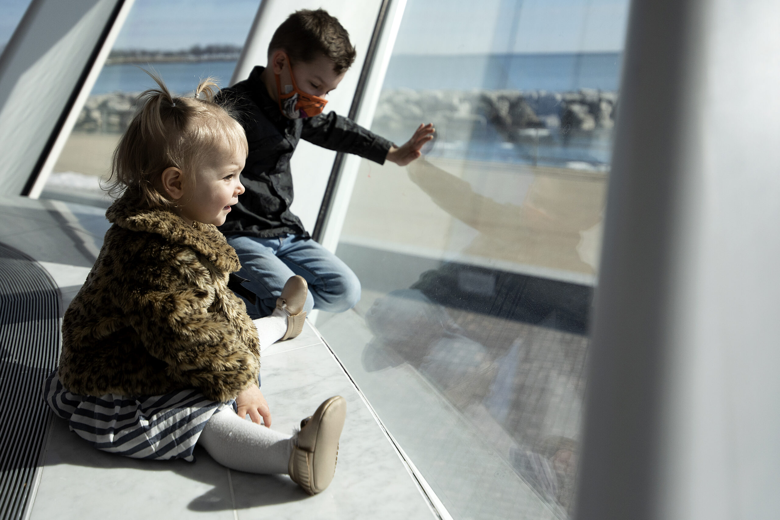 Sun shines on two children as they look out of a large window.