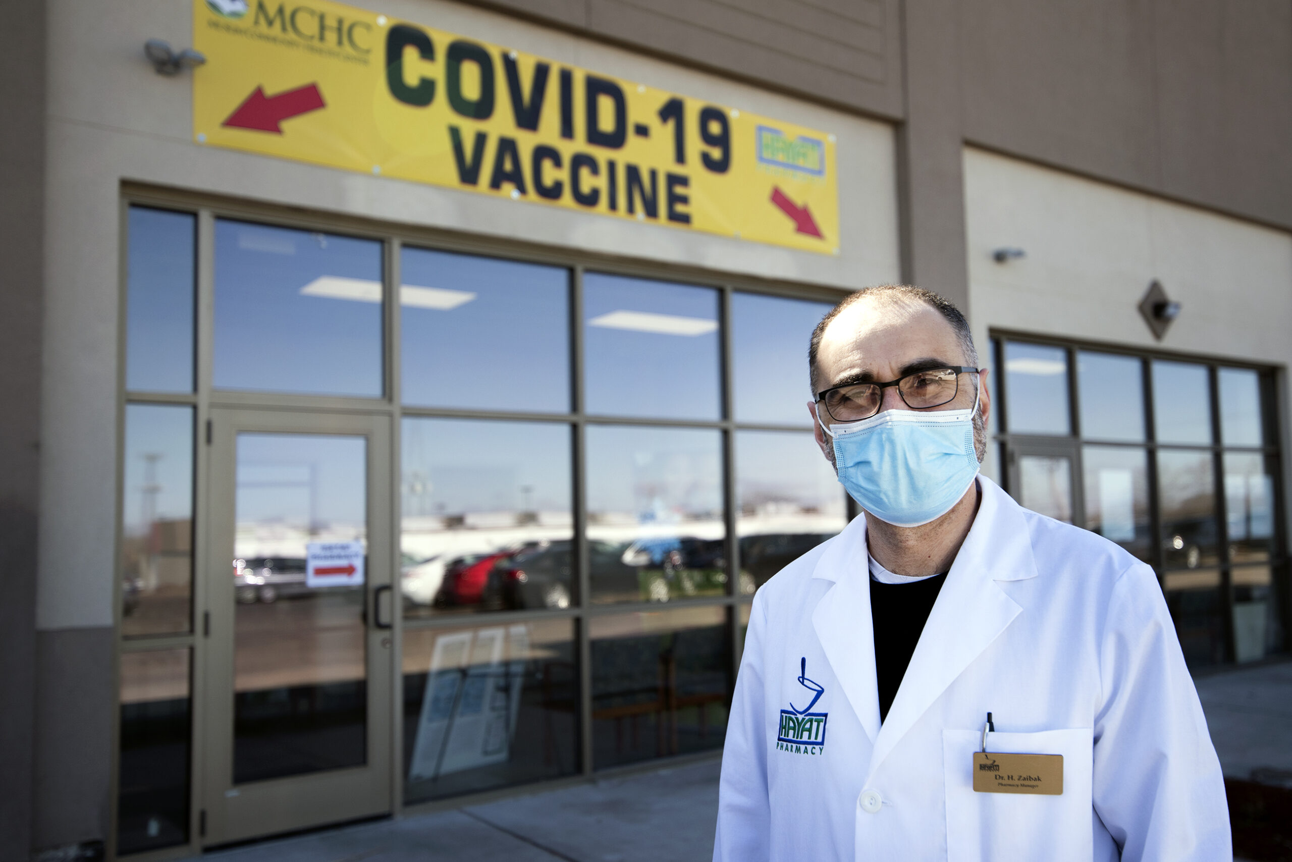 A man in a face mask stands by a yellow and red sign that says 