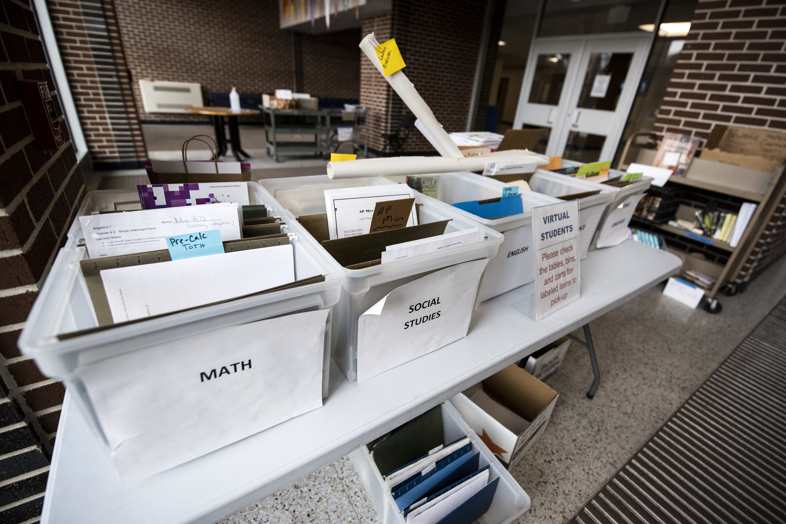 Boxes of papers in folders are placed on tables in a school lobby.