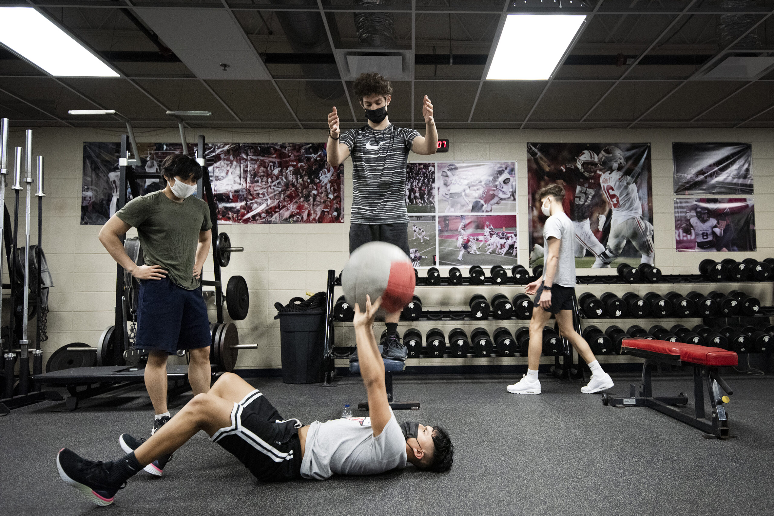 High school students wearing face masks throw a medicine ball in a PE class.