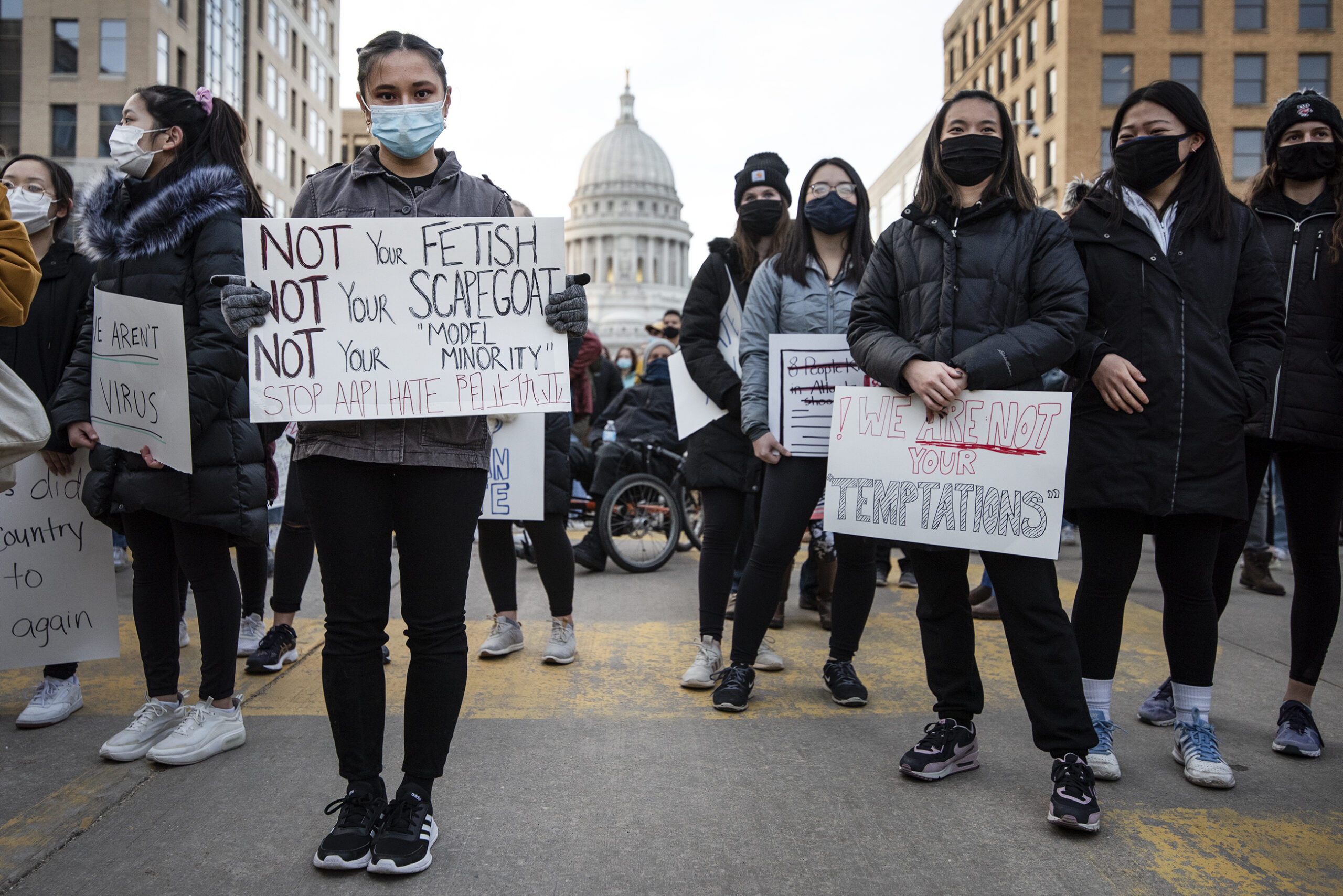 A woman makes eye contact with the camera as she holds a sign that begins 