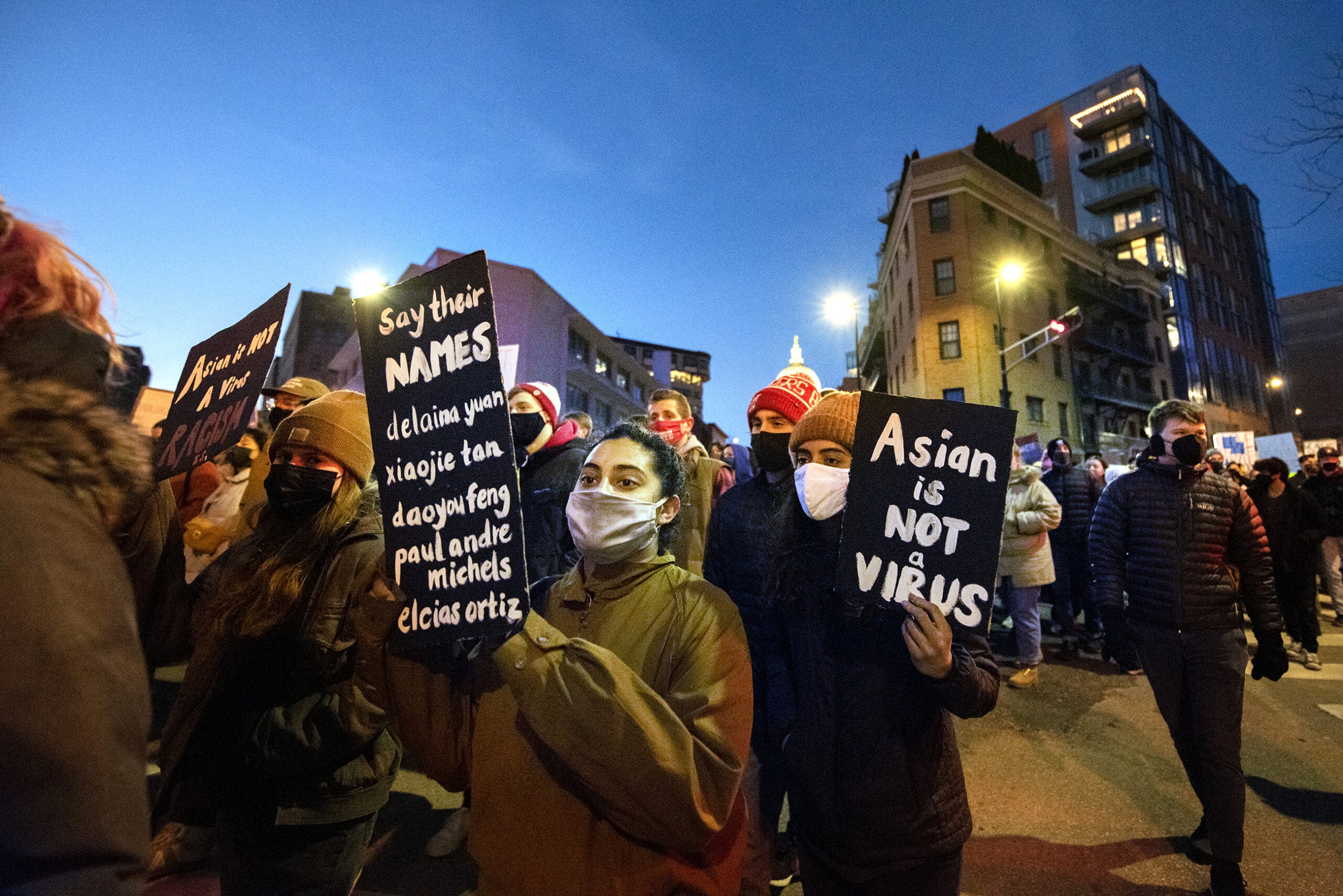 Protesters march into the night with signs as street lights shine behind them.