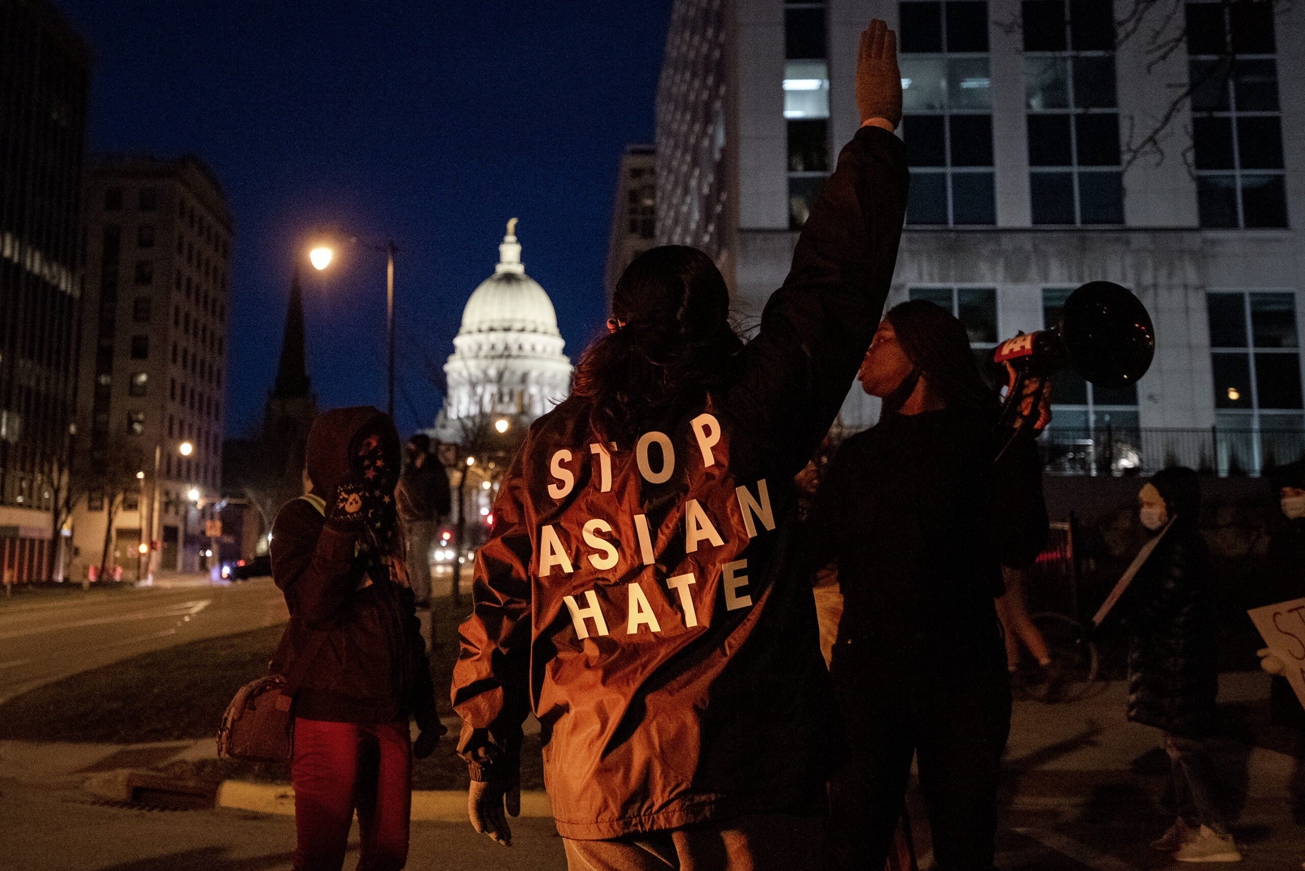"STOP ASIAN HATE" is written on the back of a protester's jacket. The Wisconsin State Capitol can be seen in the background.