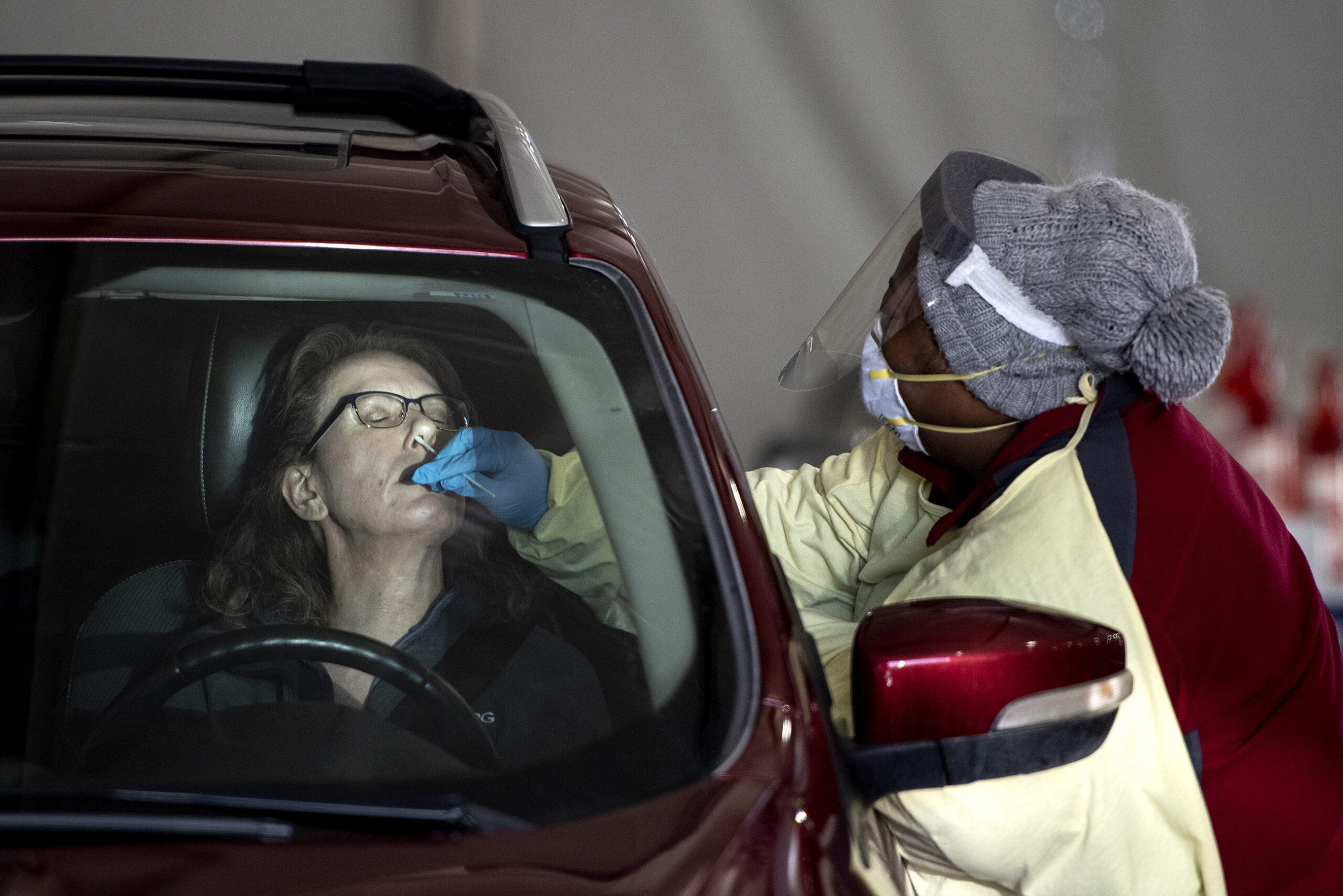 A woman leans her head back as she sits in her vehicle and is swabbed for COVID-19