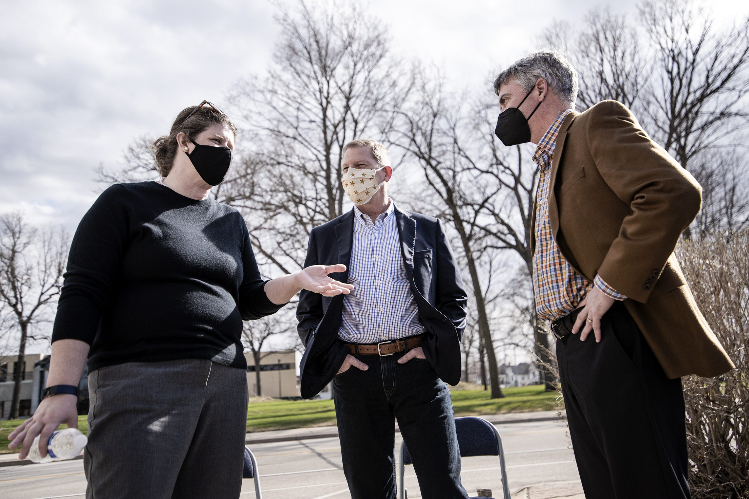 Three people wear face masks while speaking outside.