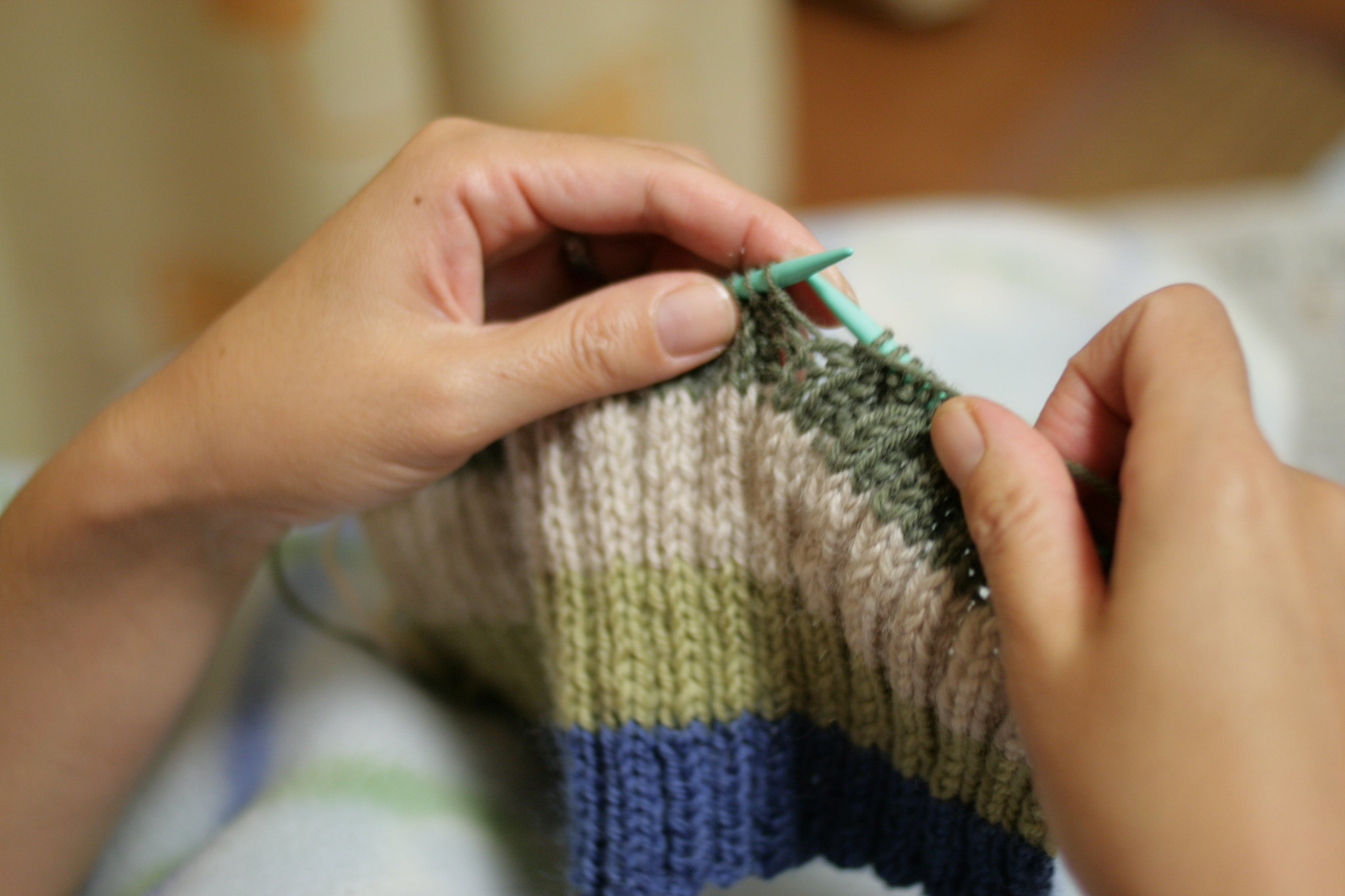 A close-up of hands holding knitting needles creating a striped knit item.