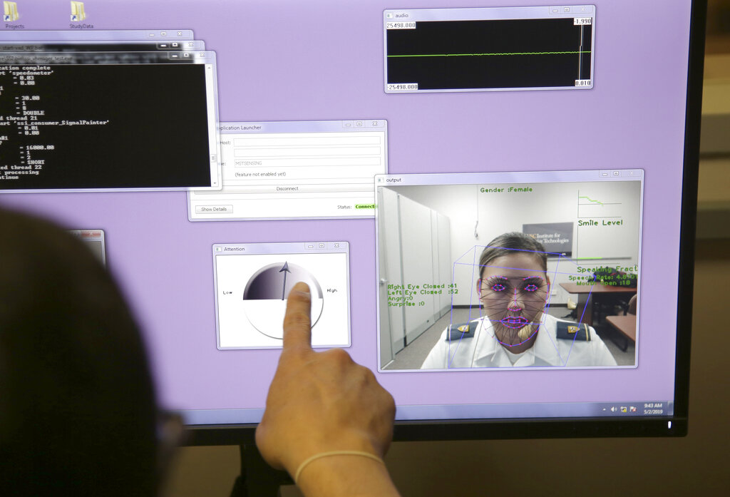A finger points at a computer screen displaying a face mapped over with different charts and graphs.