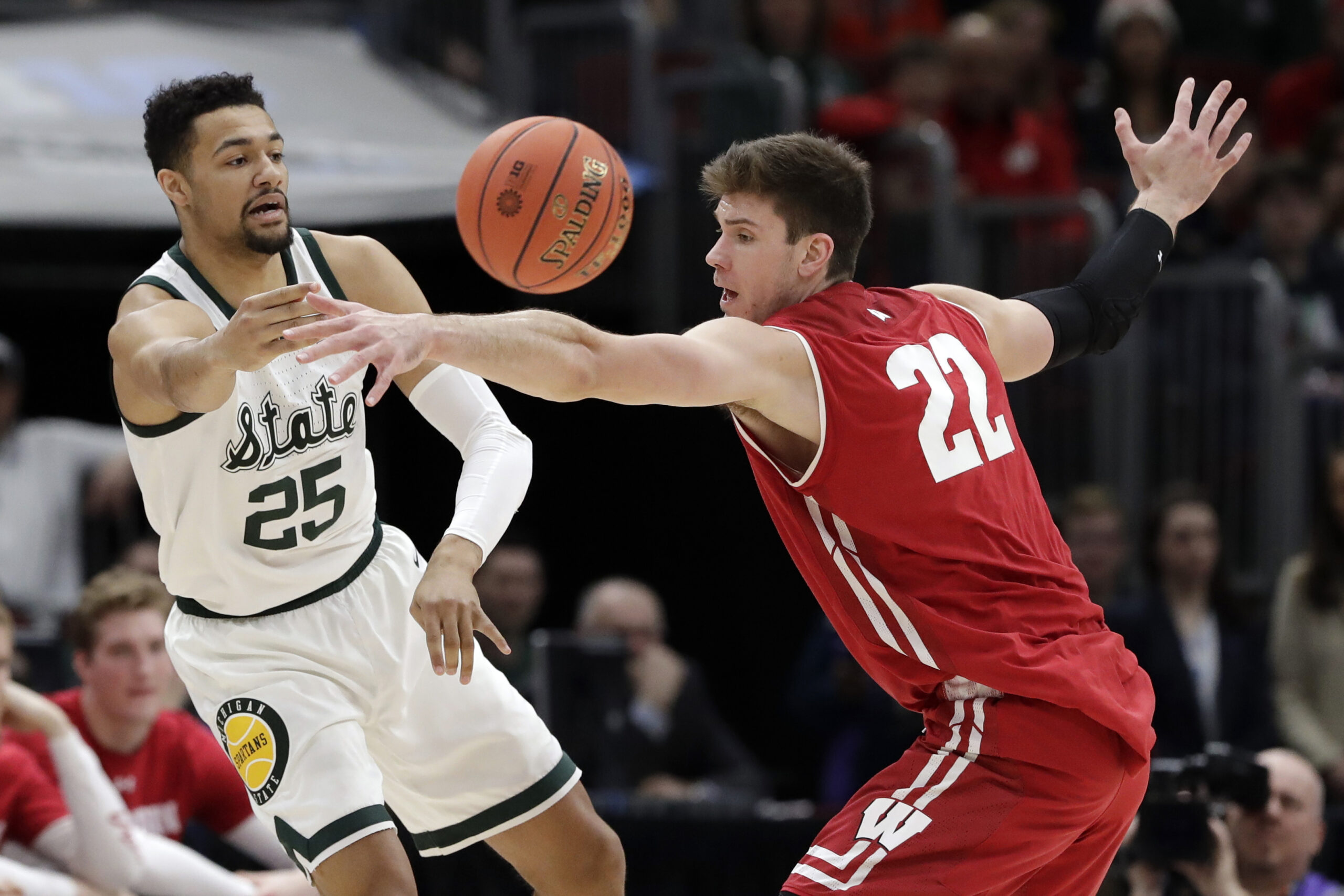 Michigan State's Kenny Goins (25) pass the ball around Wisconsin's Ethan Happ (22) during the first half of an NCAA college basketball game in the semifinals of the Big Ten Conference tournament