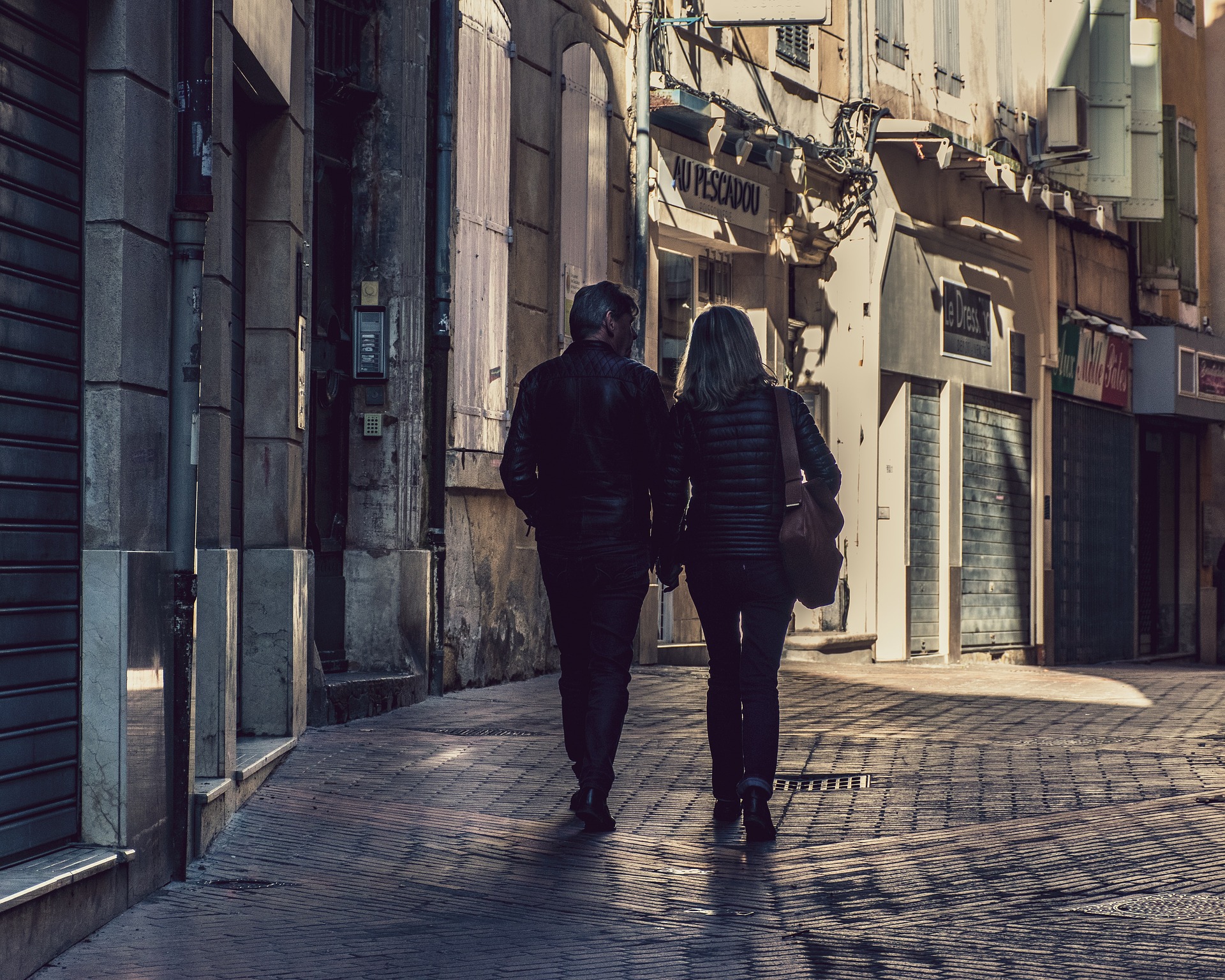 Two people walk down a cobble-stoned alleyway holding hands.