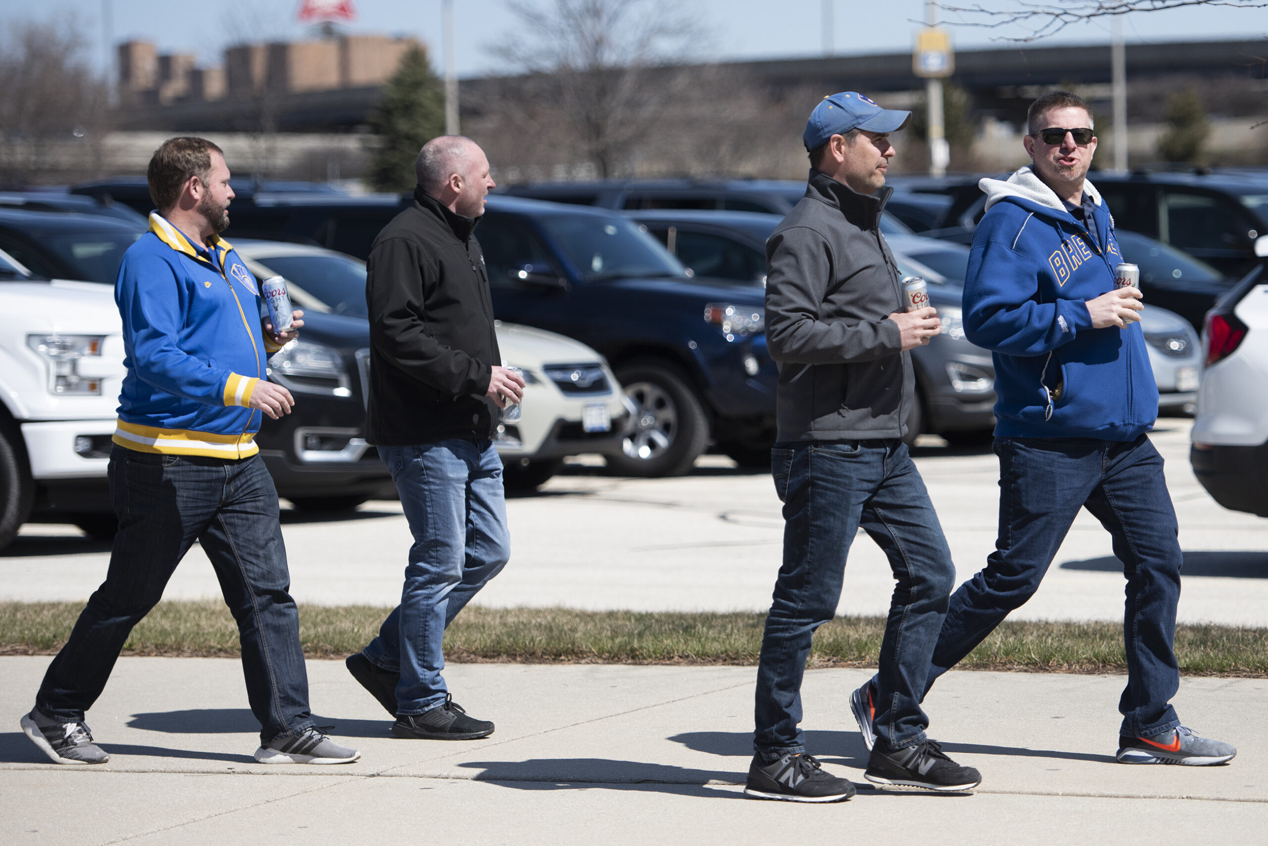 Four men hold cans of beer as they walk to the game.