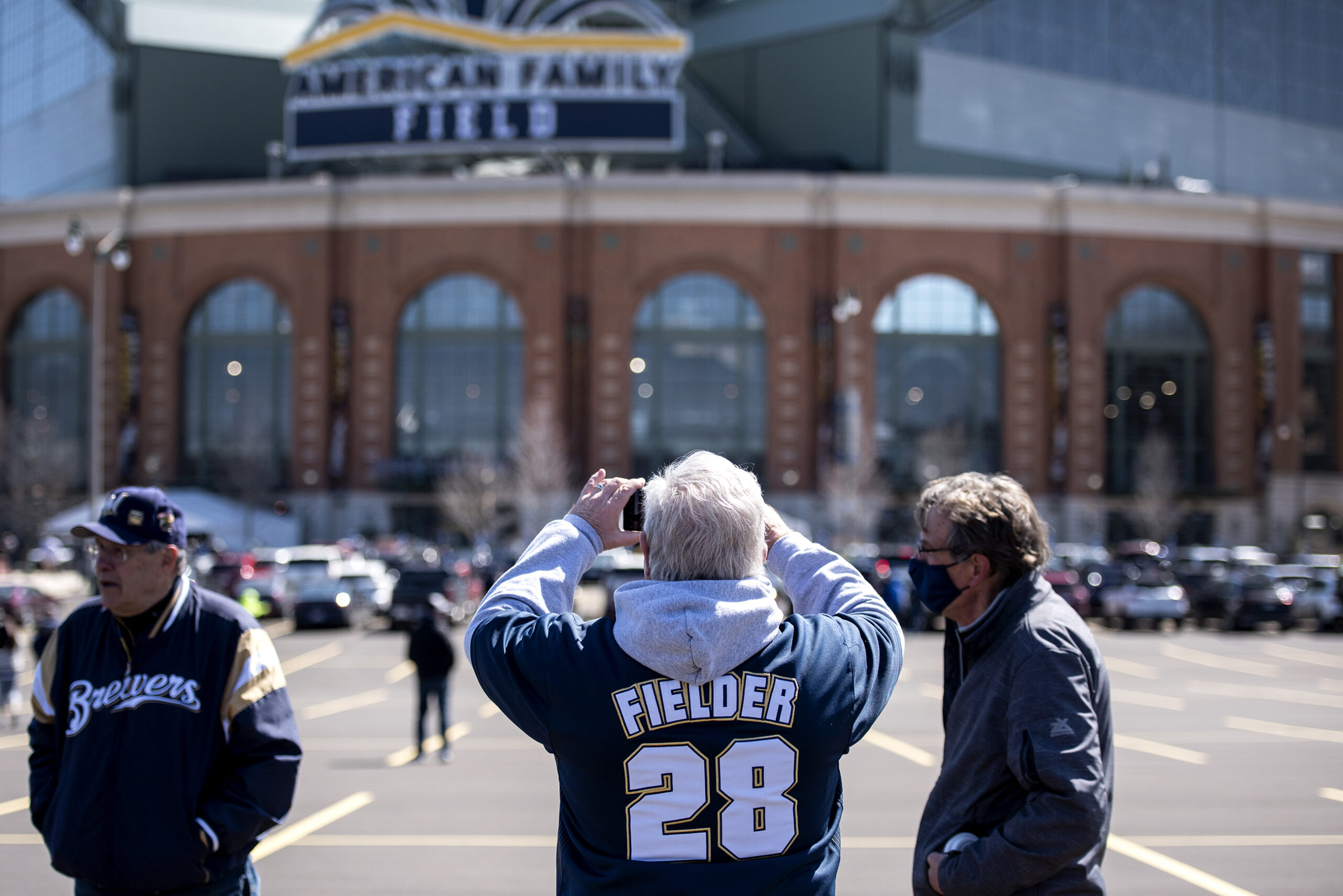 Three fans stand in the parking lot in front of American Family Field