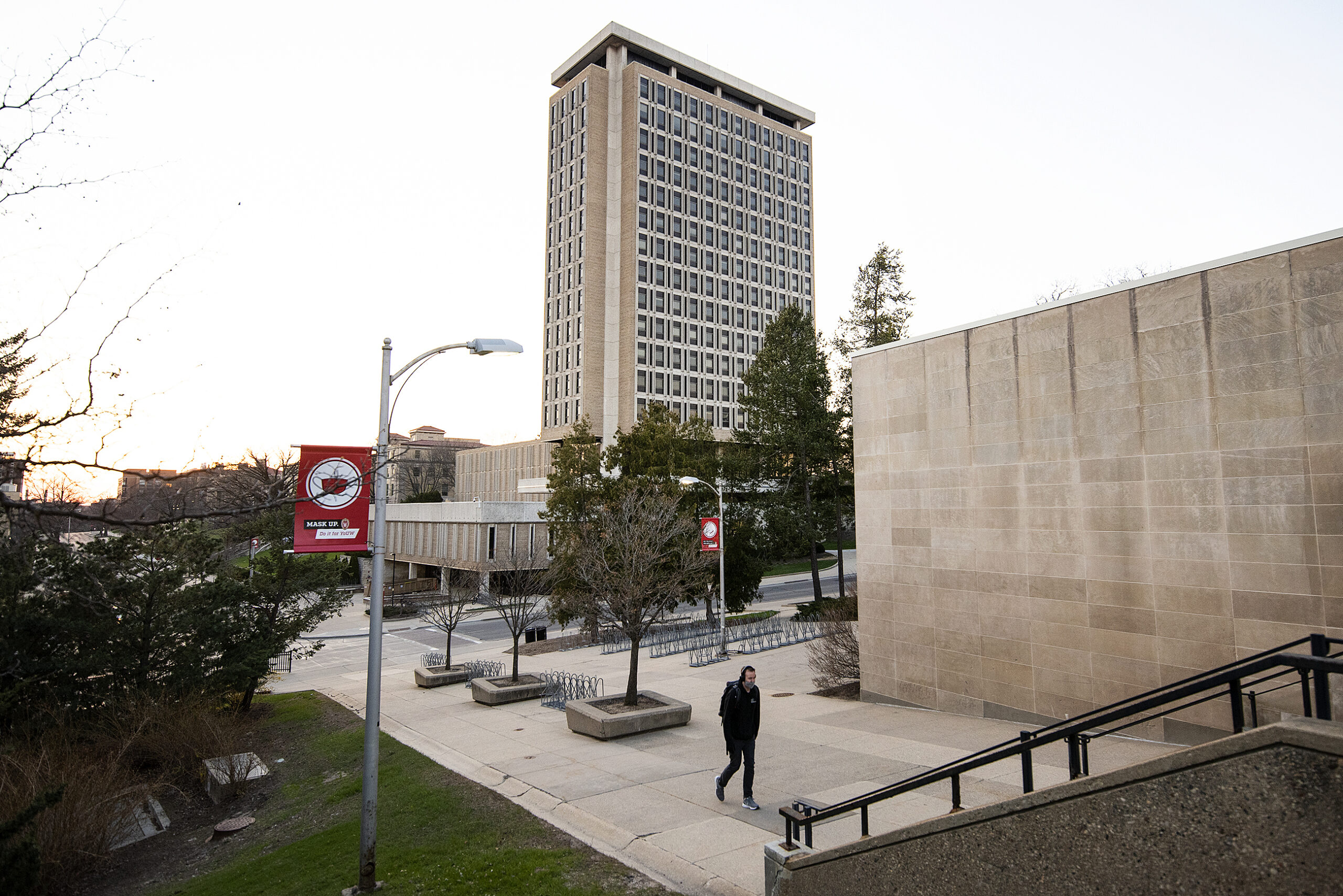 A pedestrian walks on a sidewalk near Van Hise Hall