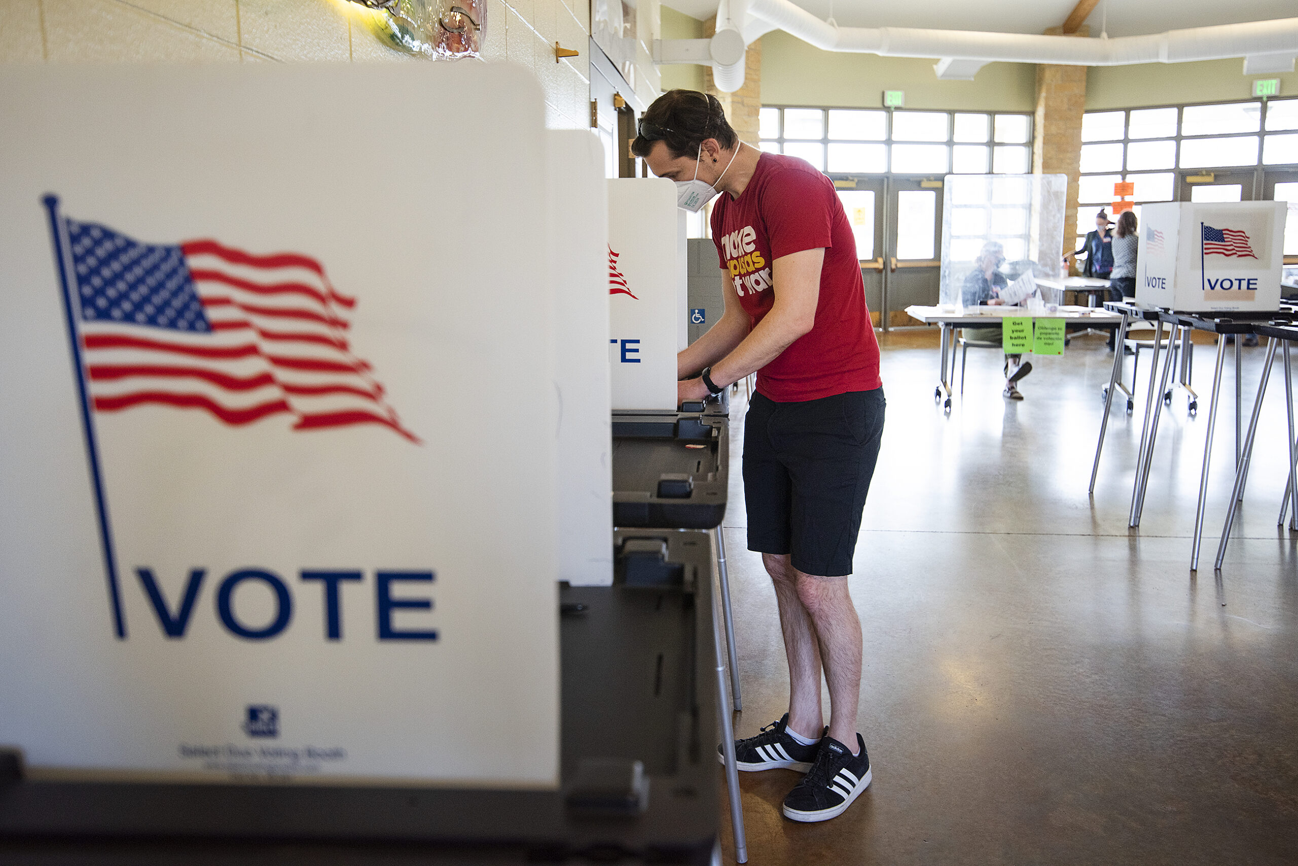 A voter in a red t-shirt fills out a ballot.