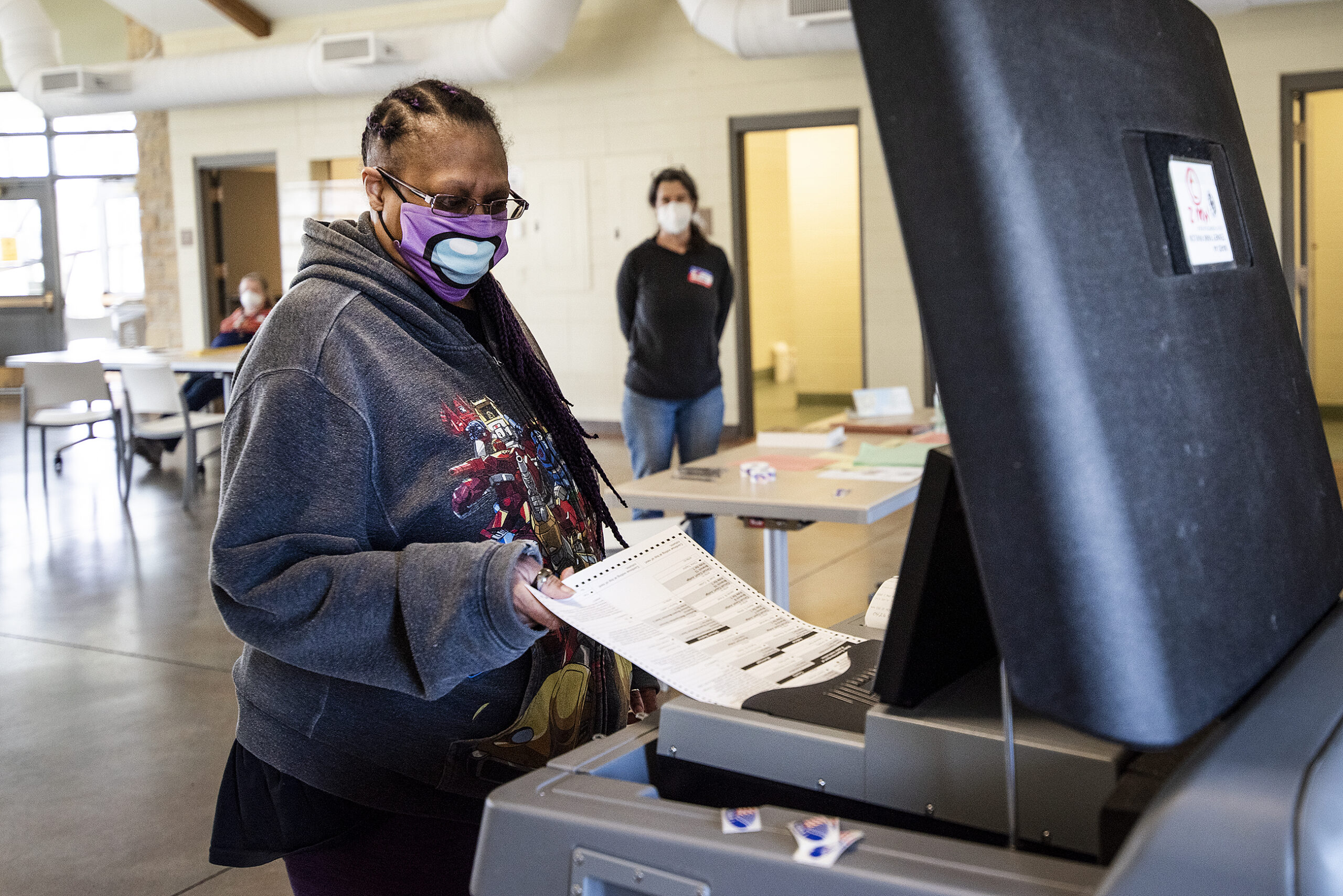 A voter in a face mask puts a ballot into the machine.