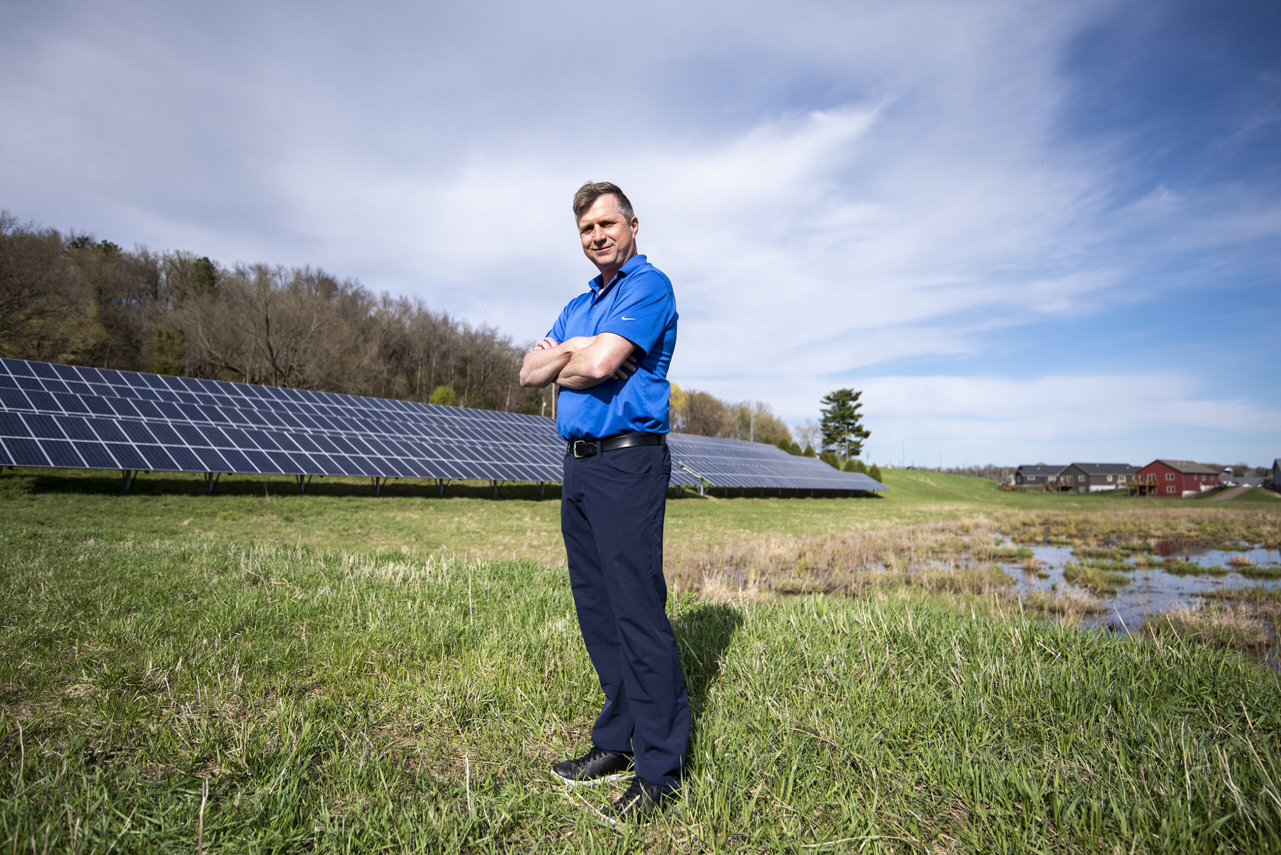 A man stands on green grass in front of a row of solar panels.