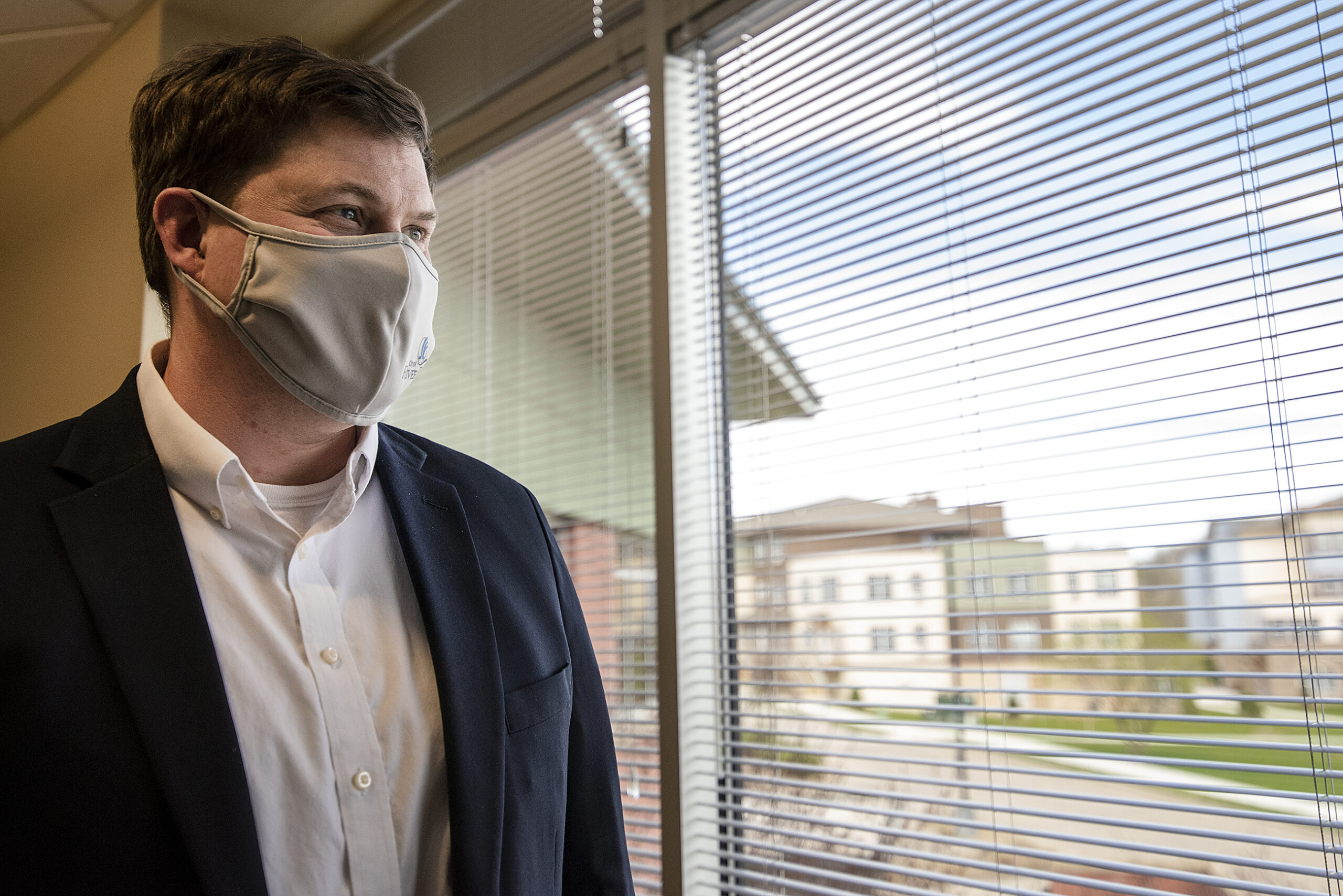 A man in a face mask stands near a window.