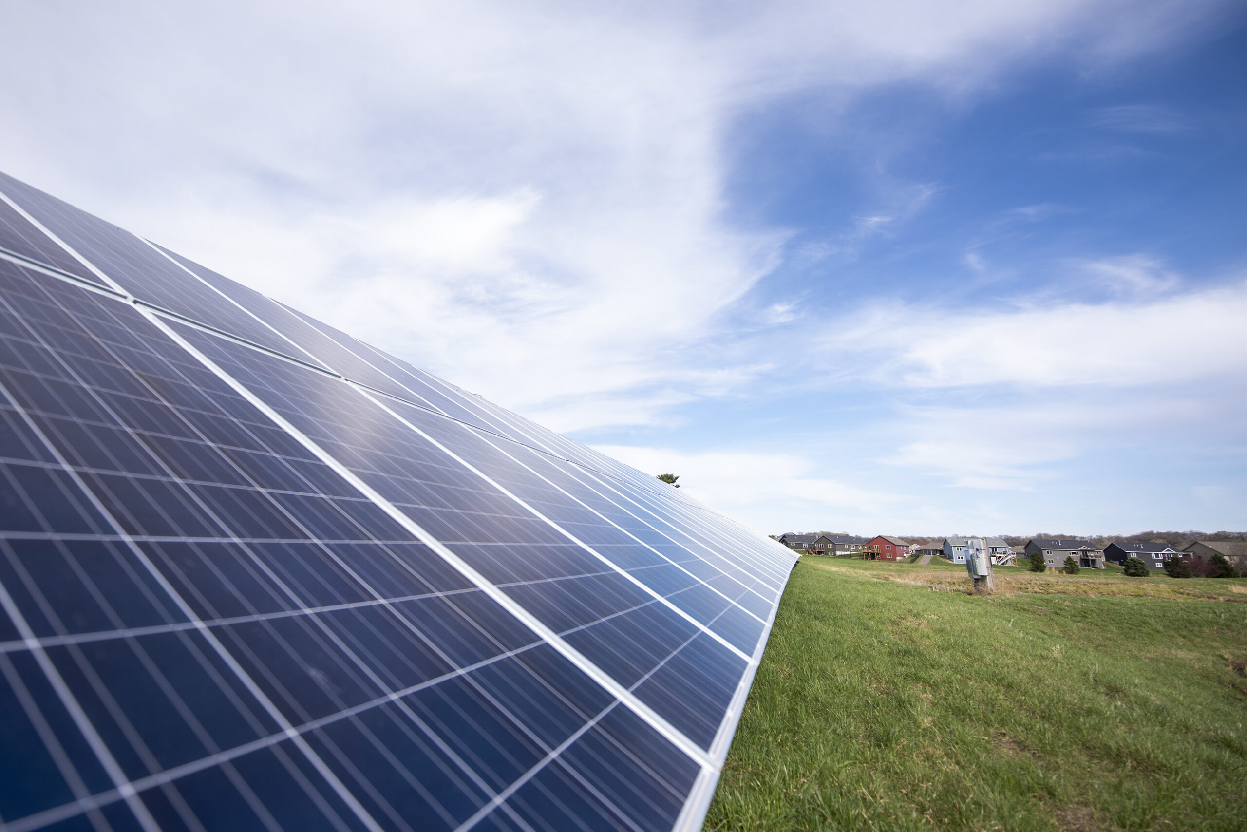 Soft white clouds, a blue sky, and green grass surround a large solar panel.