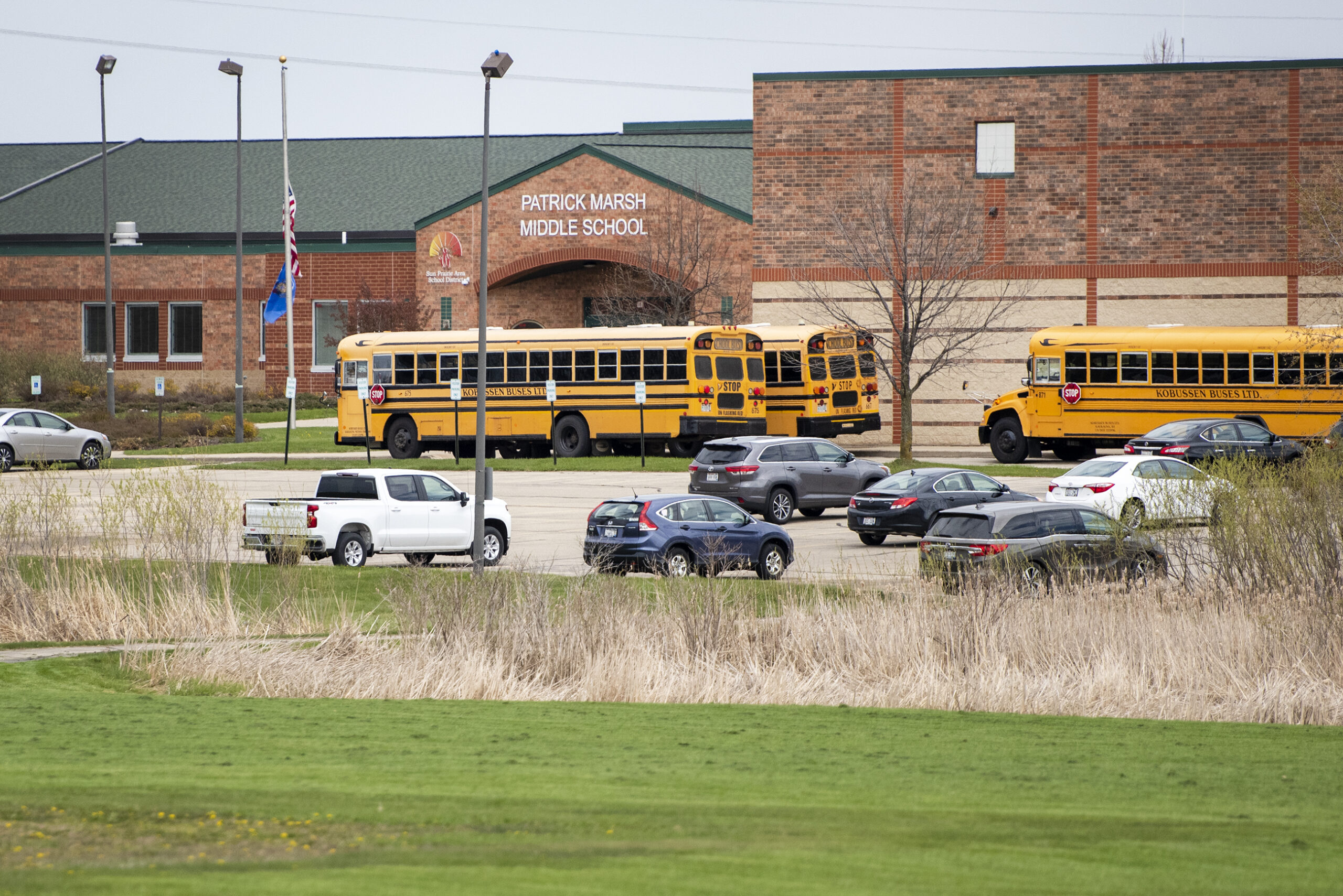 Three yellow school buses are parked in front of a brick school building.
