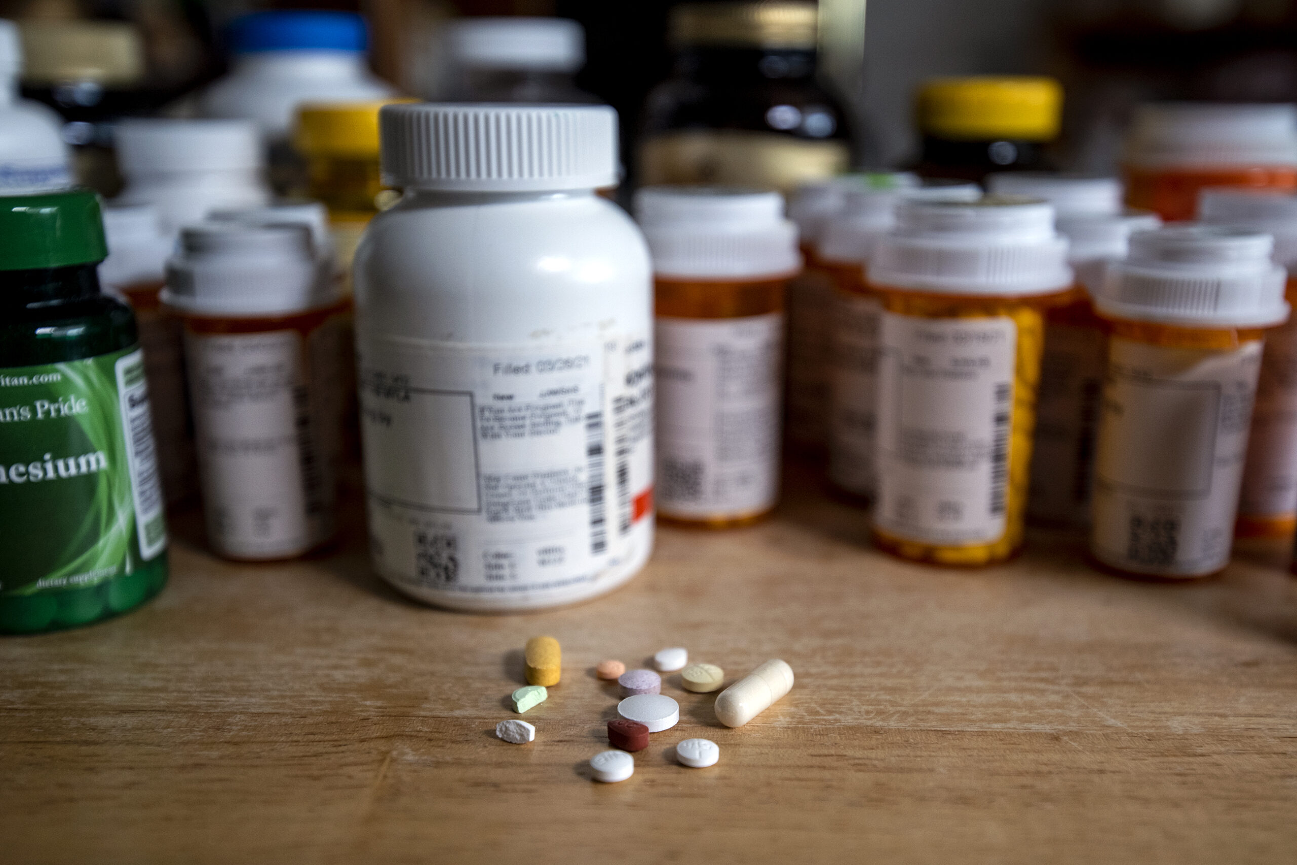 Different kinds of pills sit on a surface in front of pill bottles.
