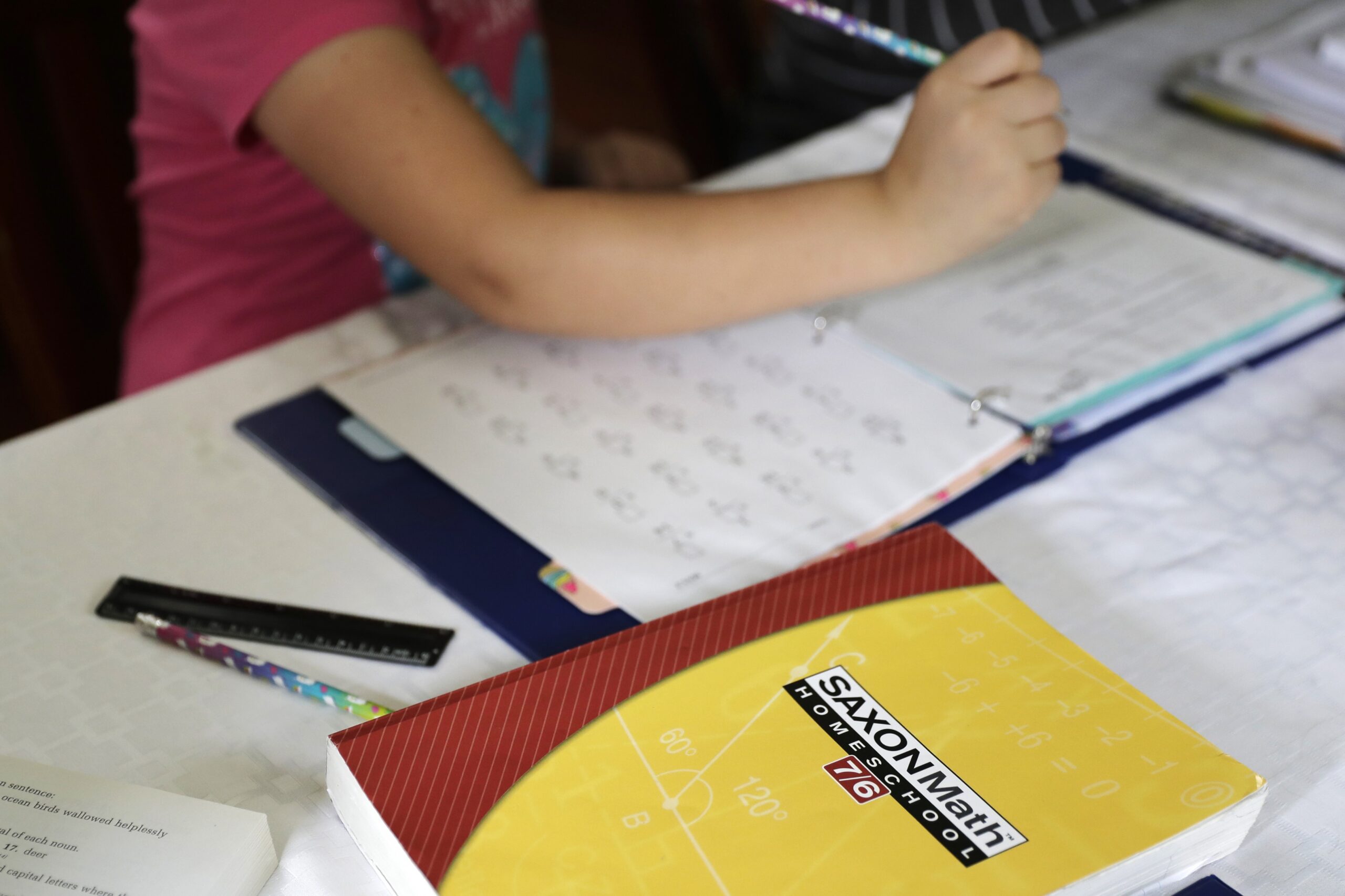 a homeschool math textbook rests on the table where Mabry Grant, 8, works on a lesson with her mom, Donya Grant