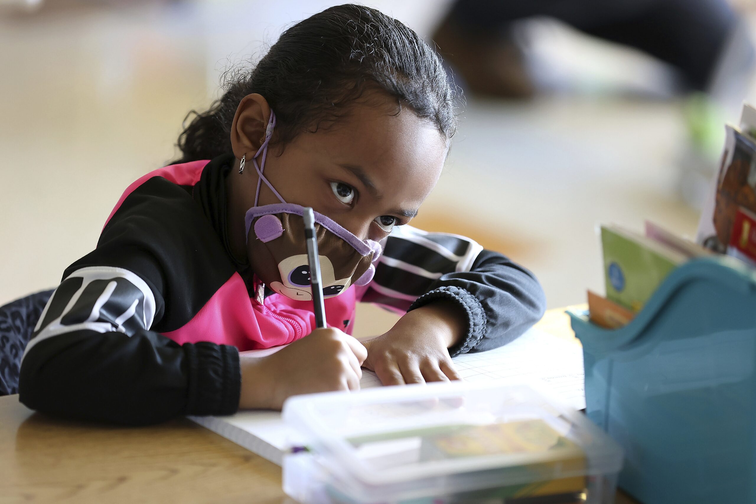 Cali Greenwood, a first-grader wearing a mask, looks up at her teacher