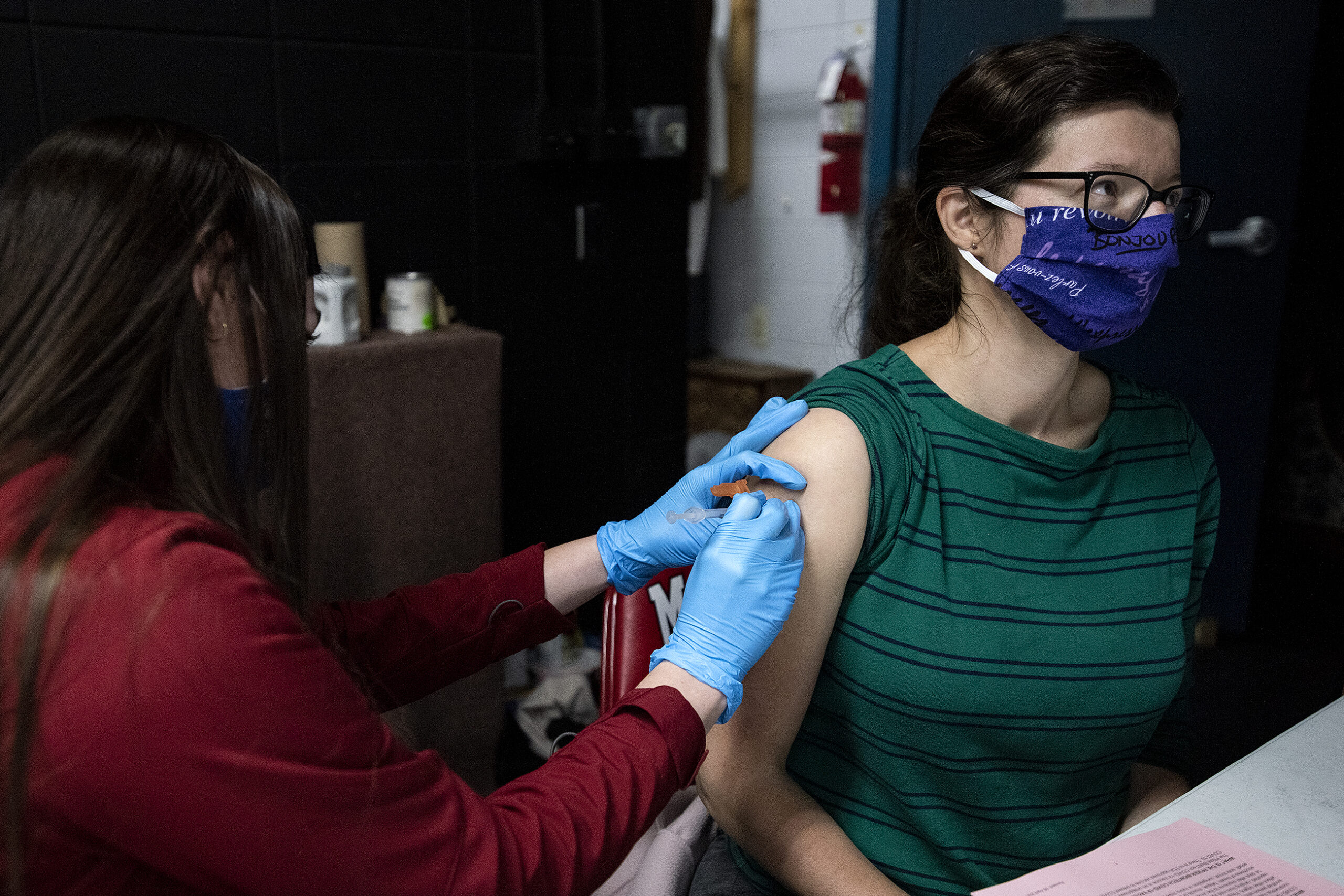 A woman with a rolled up sleeve receives a vaccine from a woman wearing blue gloves.