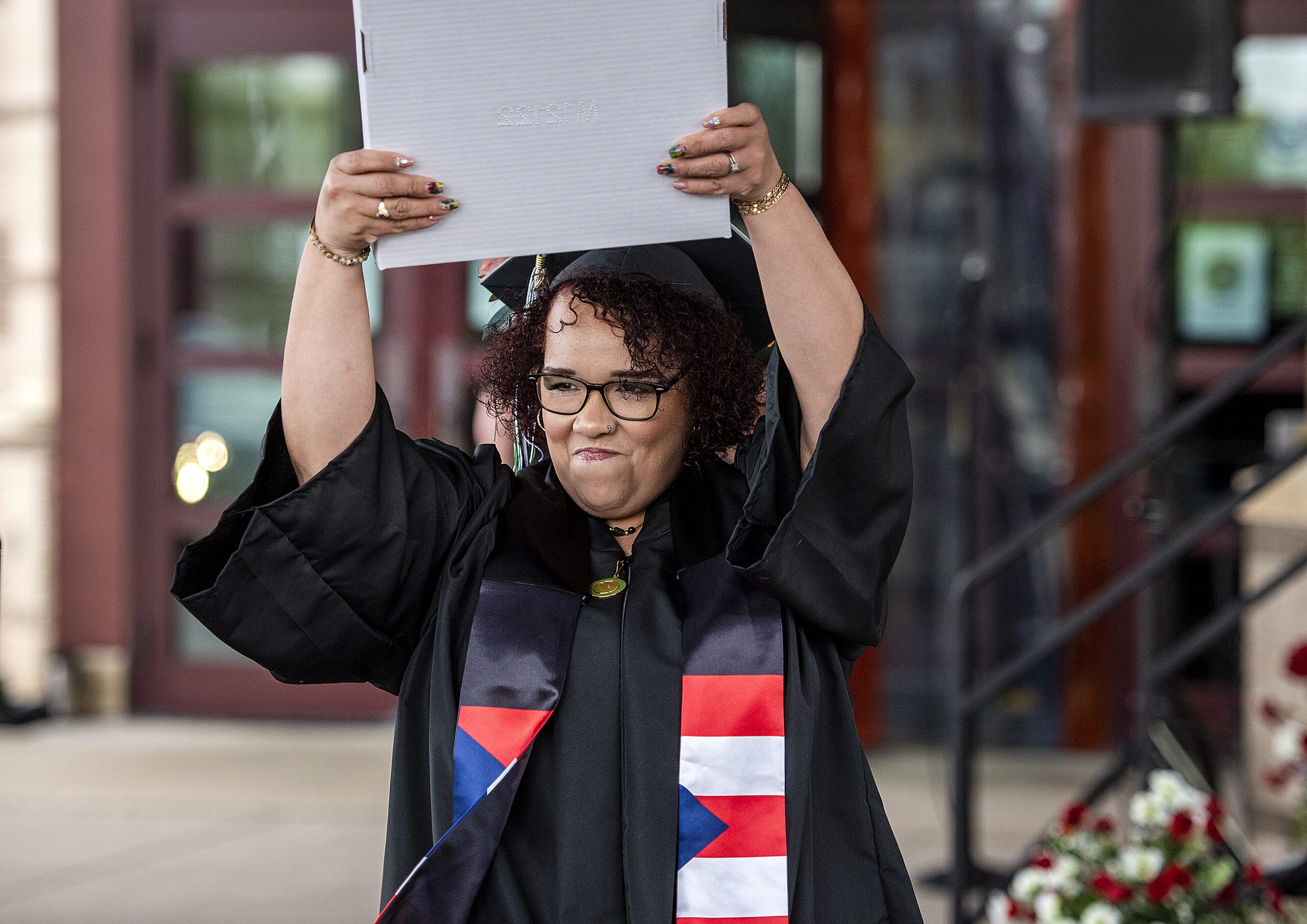 A graduate holds a diploma above her head with a determined expression.