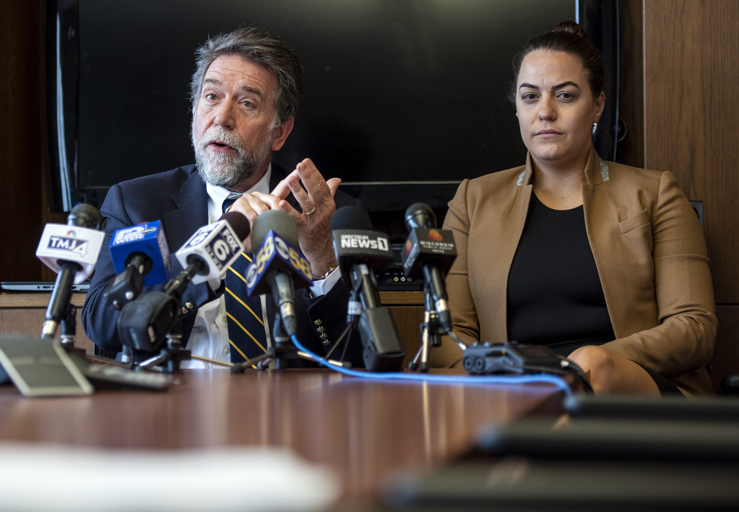 Two people sit behind several microphones while answering questions.