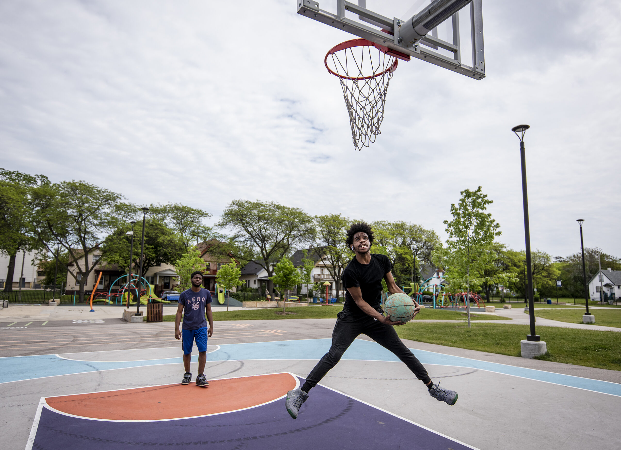 A man runs up to the basketball goal holding a basketball outdoors at a park.