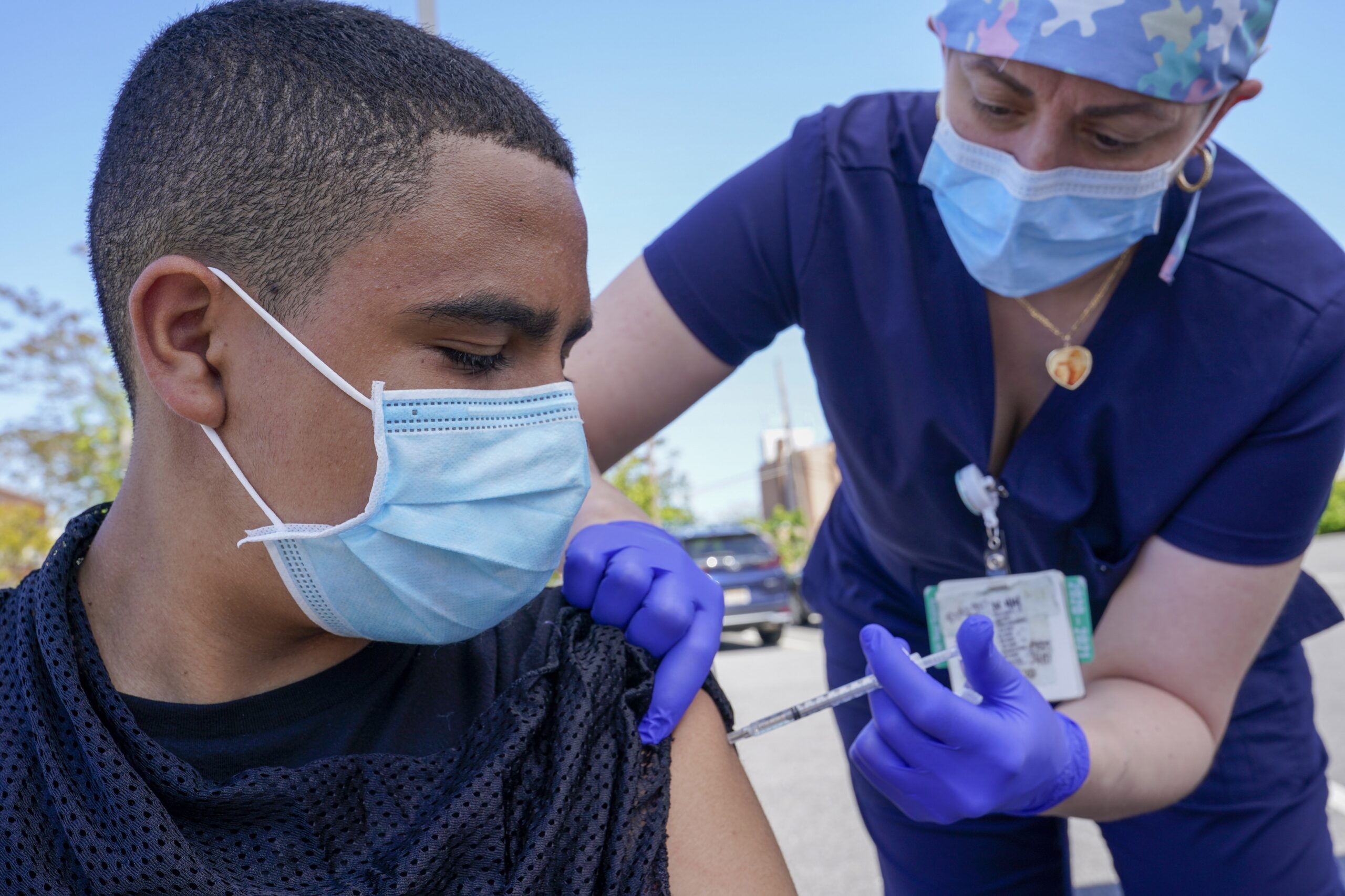 Justin Bishop watches as Registered Nurse Jennifer Reyes inoculates him with the first dose of the Pfizer COVID-19 vaccine
