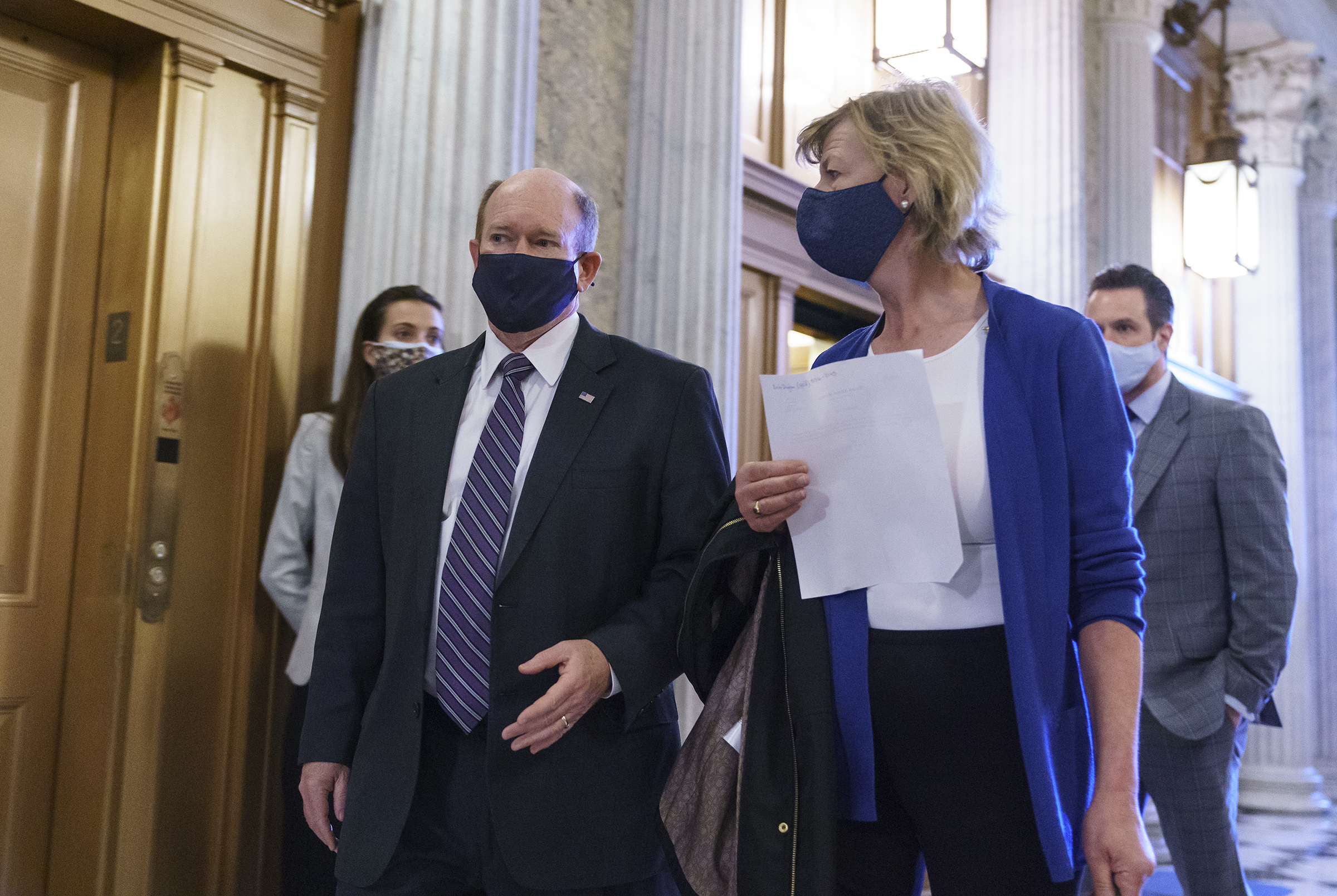 Chris Coons and Tammy Baldwin walk in a hallway wearing masks
