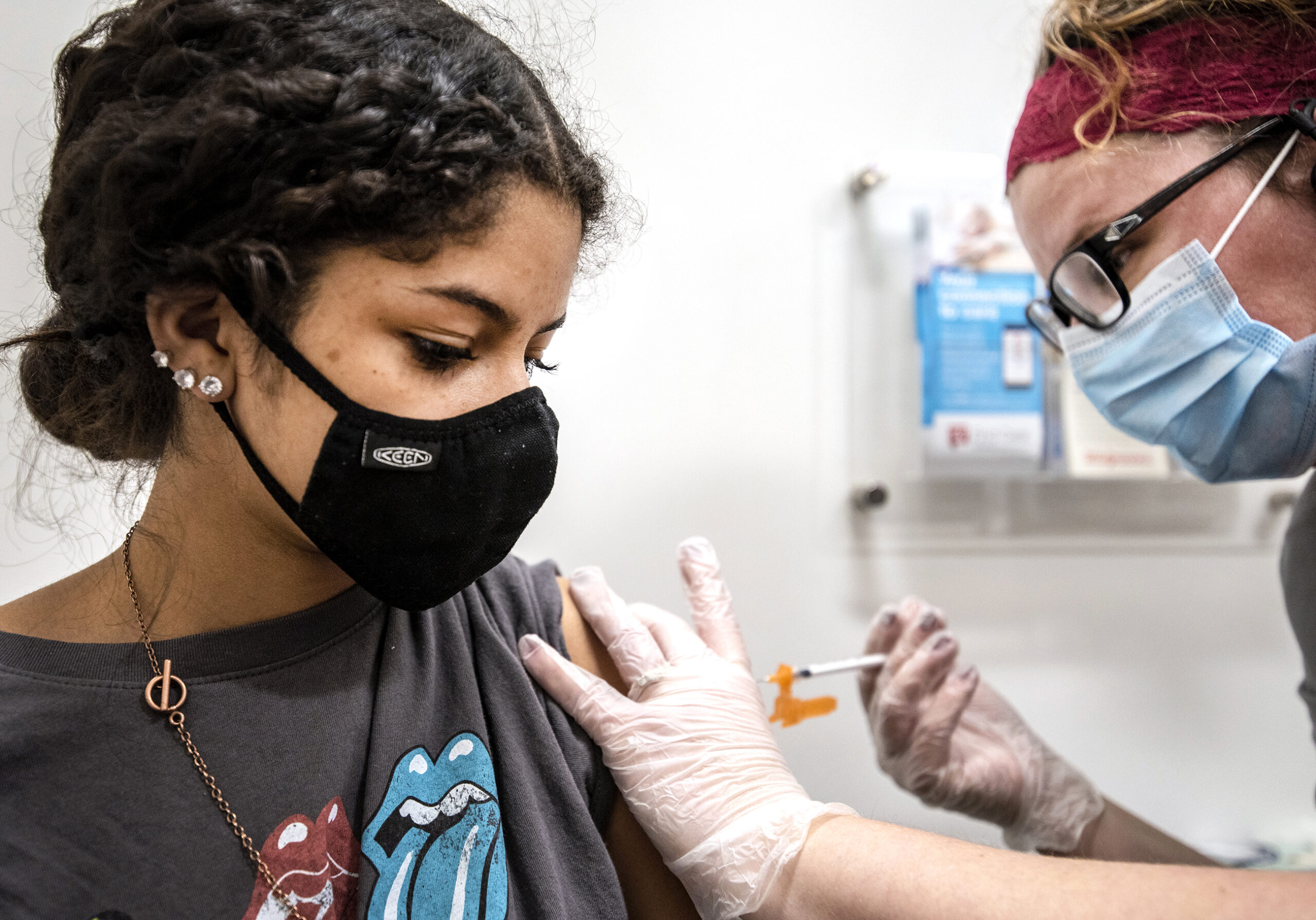 A girl looks down as a nurse pushes a COVID-19 vaccine into her arm.