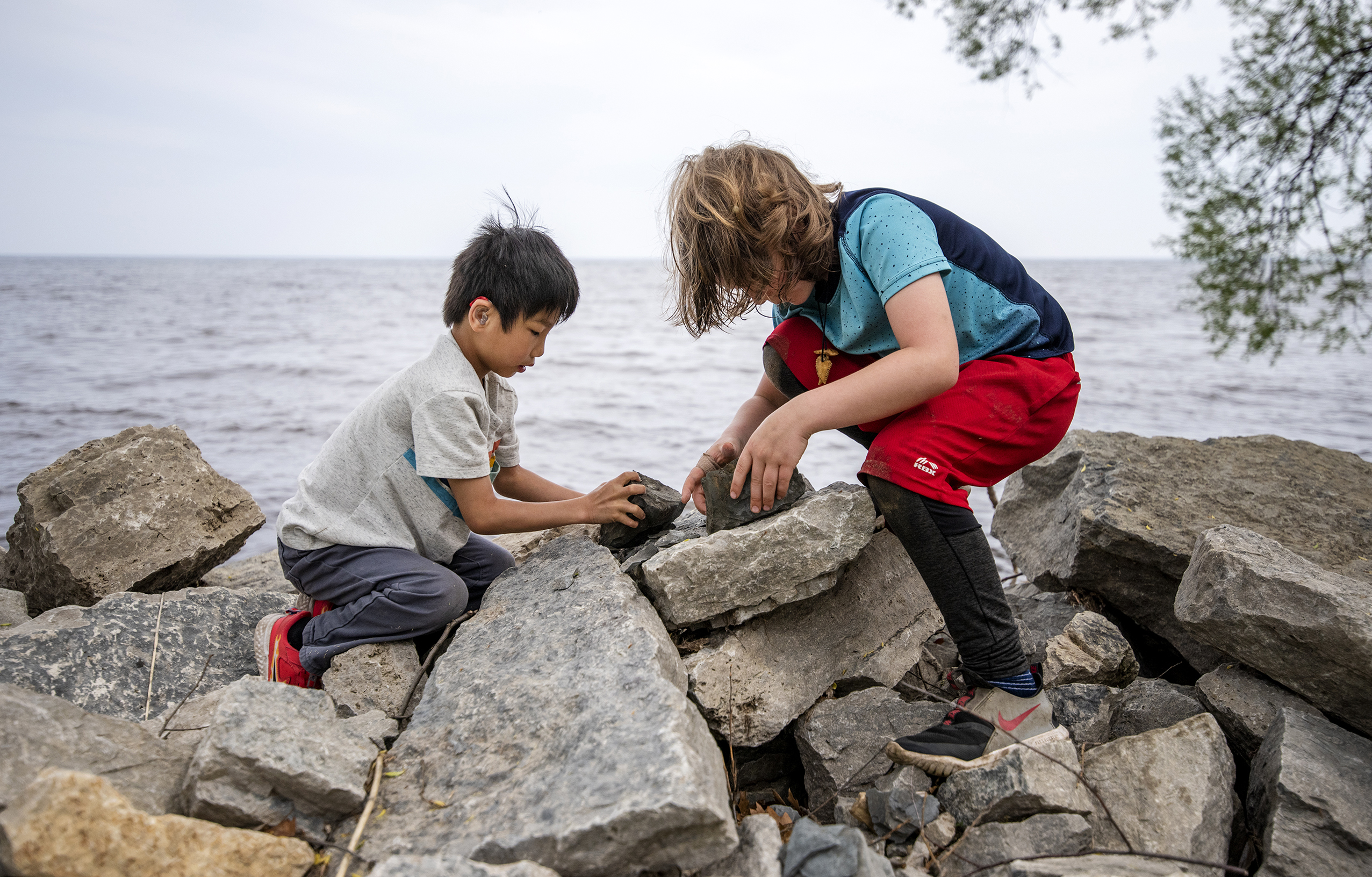 Two children play on tall rocks near the water.